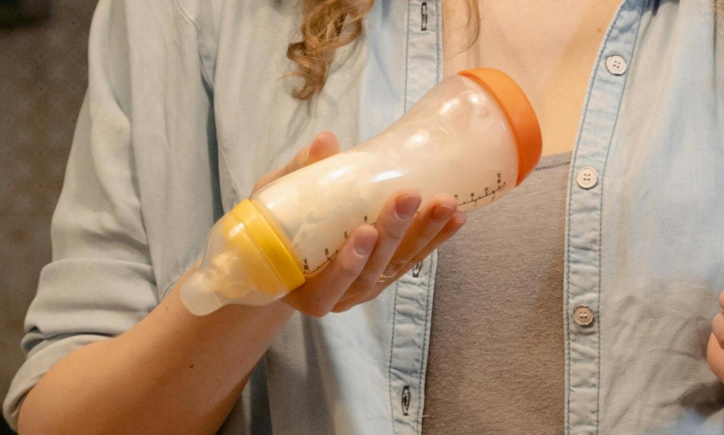 Eine Frau in einem Jeanshemd hält eine mit Milch gefüllte Babyflasche | Quelle: Pexels