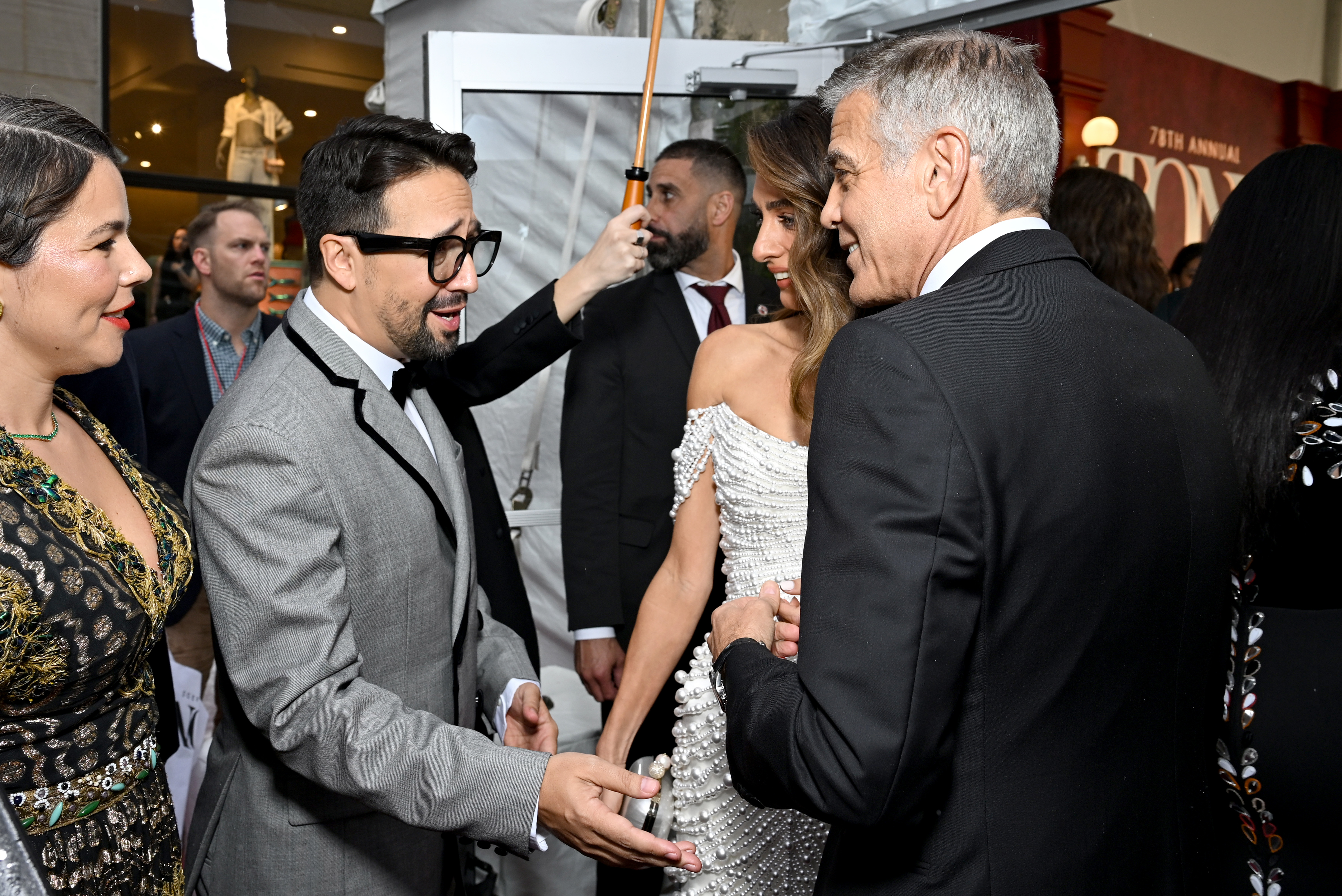 In einem offenen Gespräch unterhalten sich George Clooney und Amal Clooney mit Lin-Manuel Miranda. Amal lächelt warmherzig, während George sich angeregt unterhält und für einen lebhaften Moment unter dem roten Baldachin sorgt.