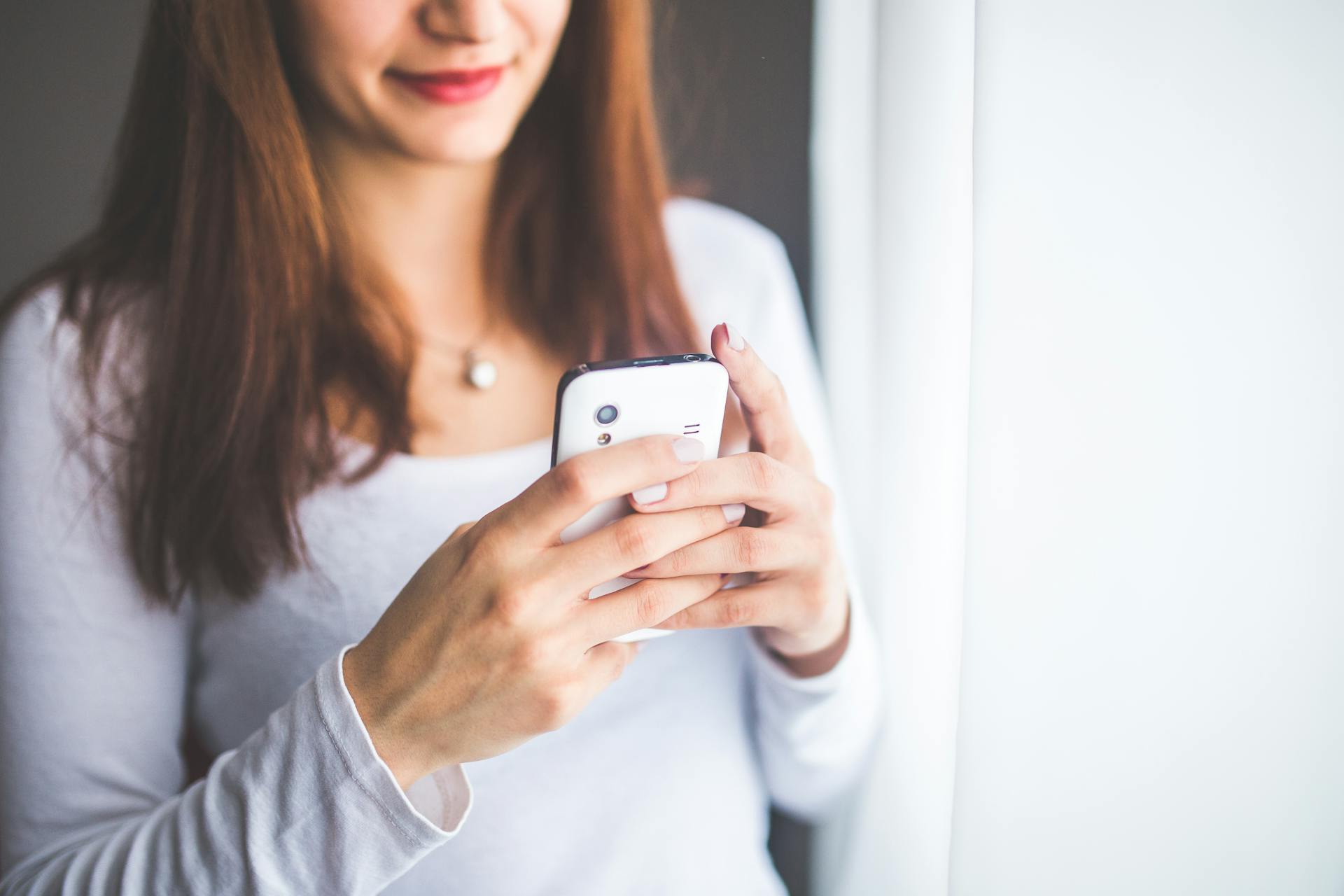 Eine lächelnde Frau, die auf ihr Telefon schaut | Quelle: Pexels