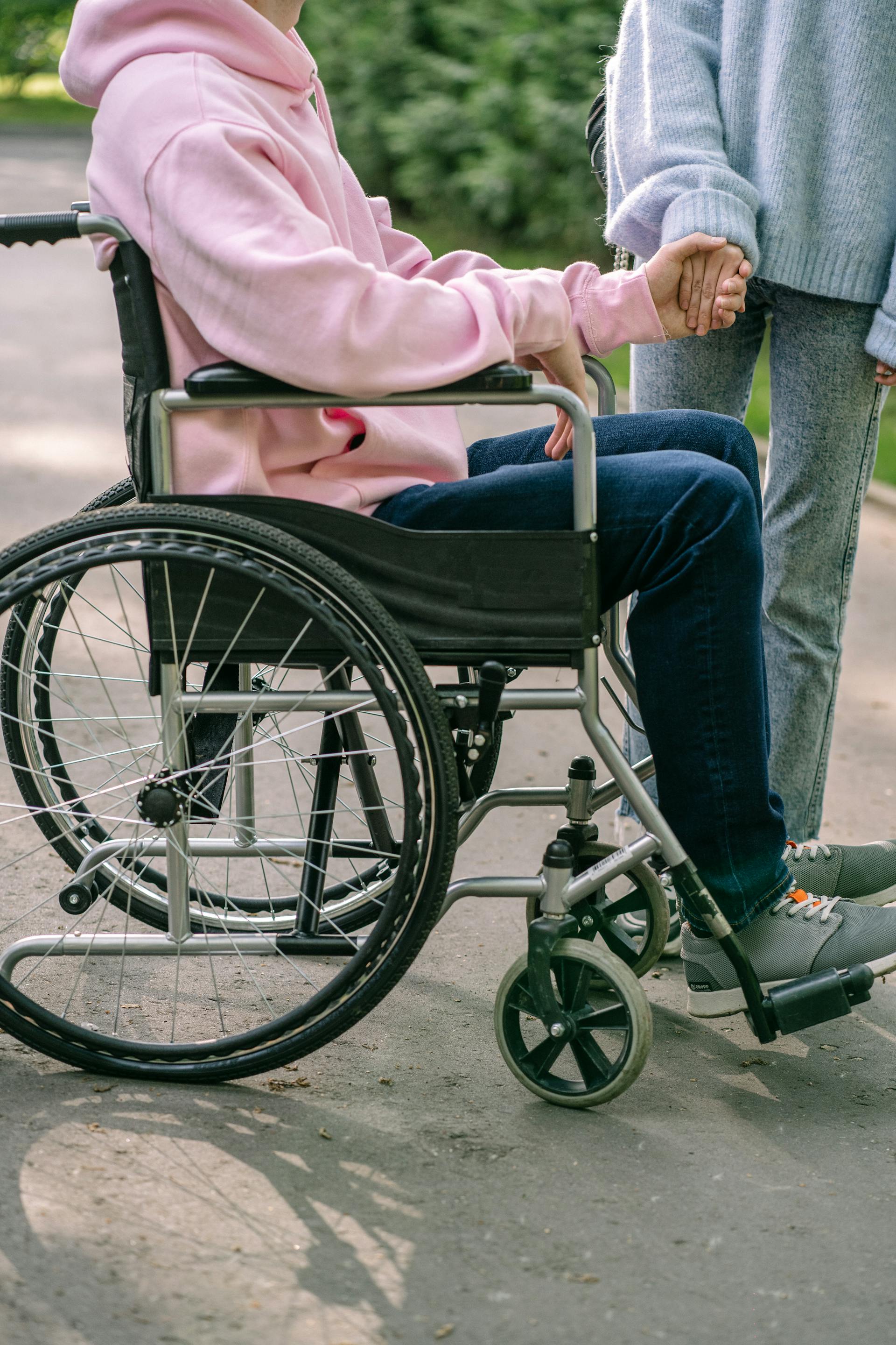 Ein Mann in einem rosa Kapuzenpulli sitzt in einem Rollstuhl und hält die Hand einer Frau | Quelle: Pexels