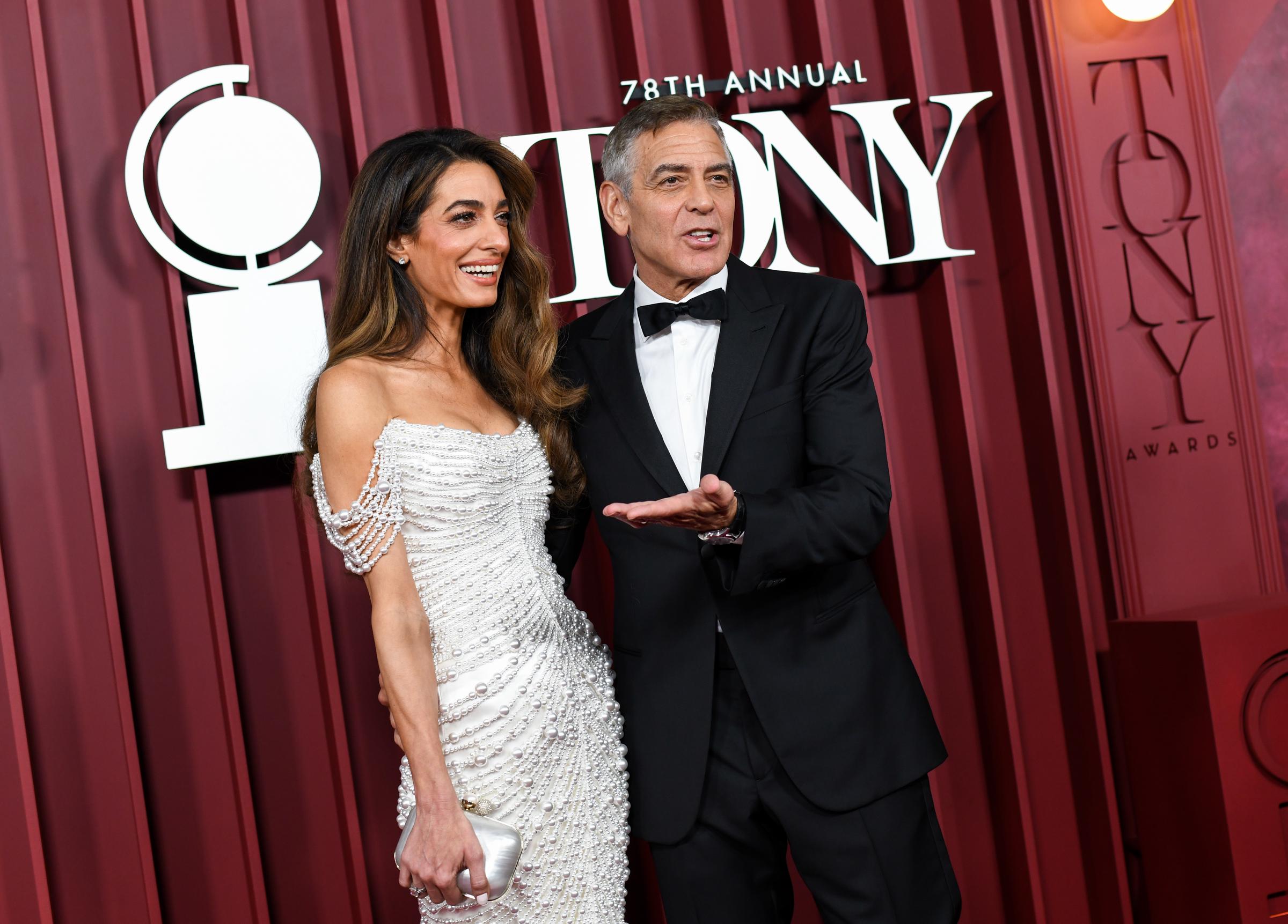 Amal und George Clooney tauschen sich bei ihrer Ankunft auf der Tony-Verleihung auf heitere Weise aus. George gestikuliert mitten im Satz, während Amal lacht und dem roten Teppich eine offene Energie verleiht.