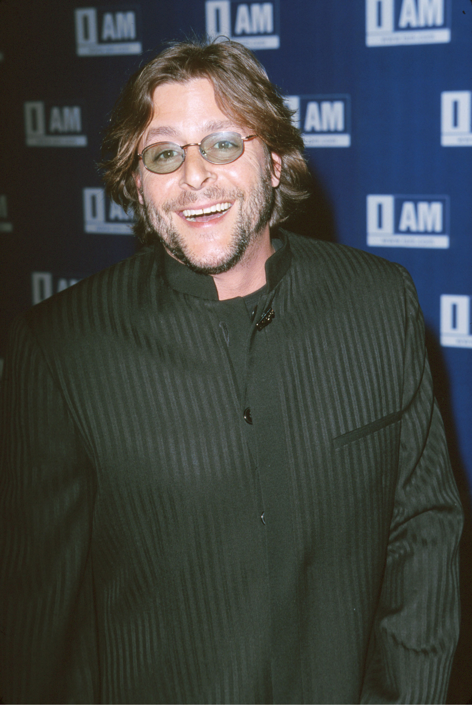 Mit einer getönten, ovalen Brille, einem Dreitagebart und einer dunklen, Nadelstreifen-Jacke mit Stehkragen lächelte der Schauspieler am 21. März 2000 auf dem roten Teppich bei der IAM.com Hollywood Launch Party in den Quixote Studios in Hollywood strahlend. | Quelle: Getty Images