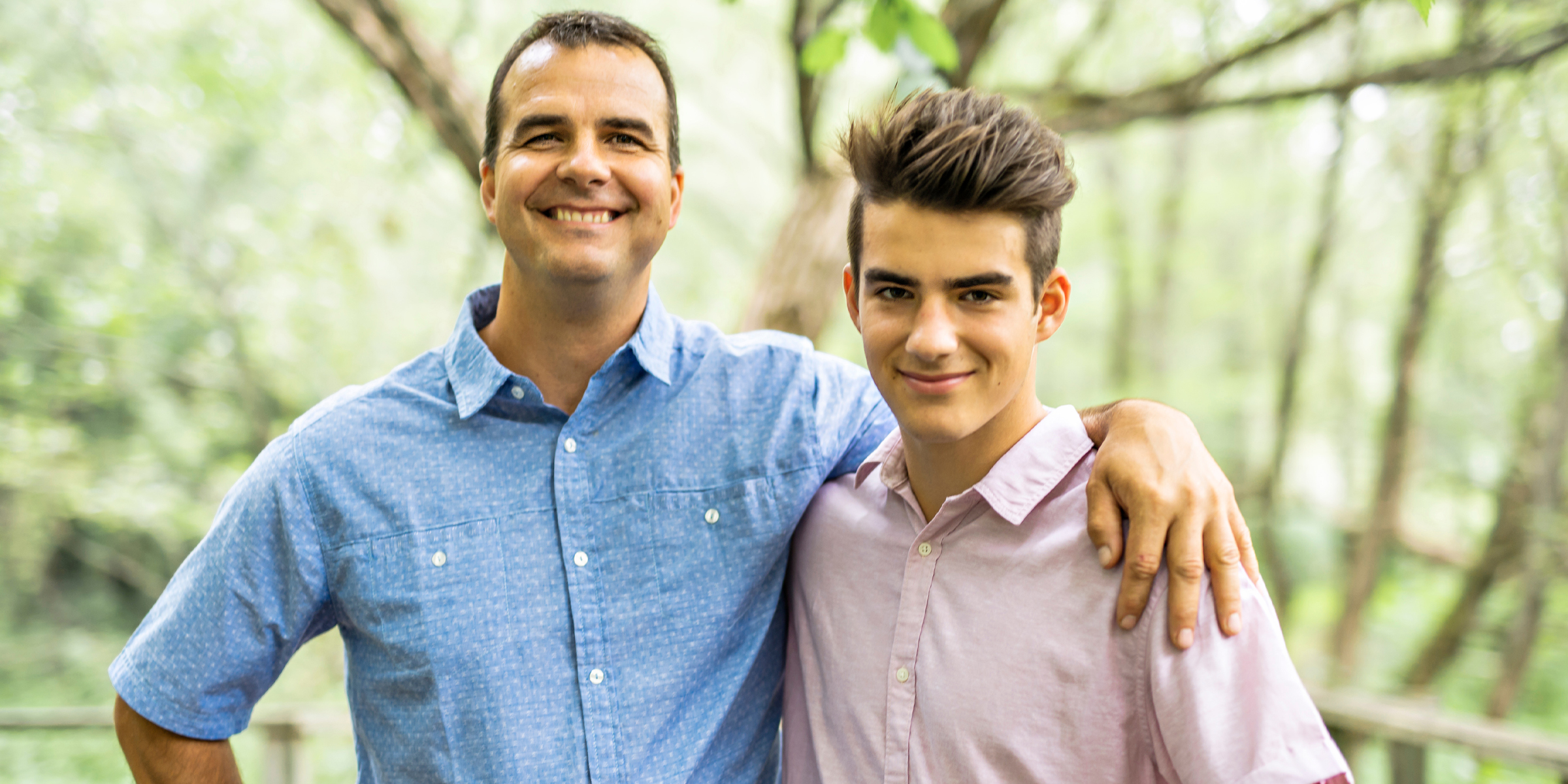 Ein lächelnder Mann und ein Teenager posieren zusammen im Freien in einem Waldgebiet | Souce: Shutterstock