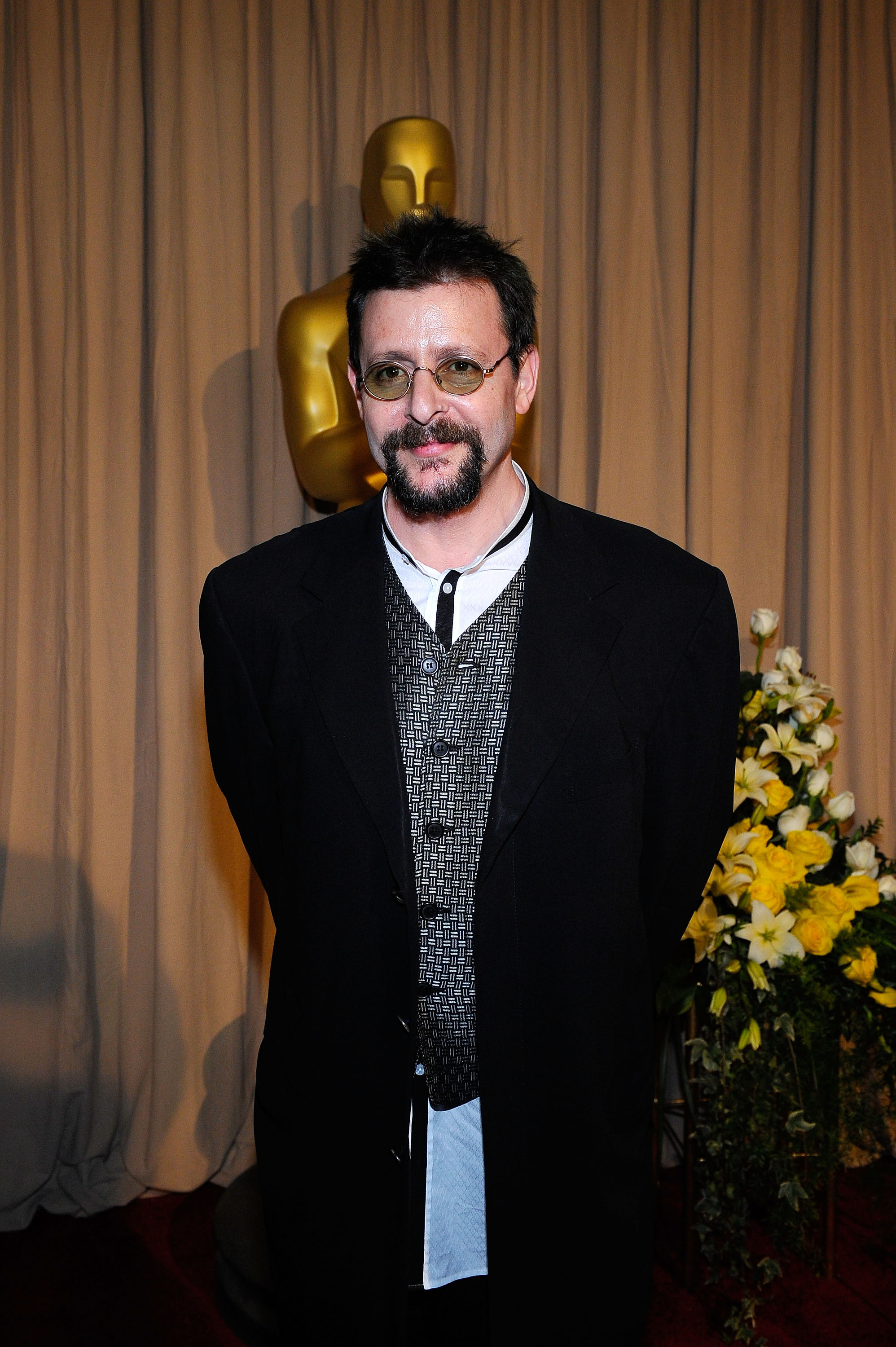 Der Schauspieler posierte am 7. März 2010 bei der 82. Oscar-Verleihung hinter der Bühne neben einer goldenen Oscar-Statuette und kombinierte eine gemusterte Weste und einen dunklen Mantel mit einer kleinen getönten Brille und einem ordentlich gestutzten Ziegenbart. | Quelle: Getty Images