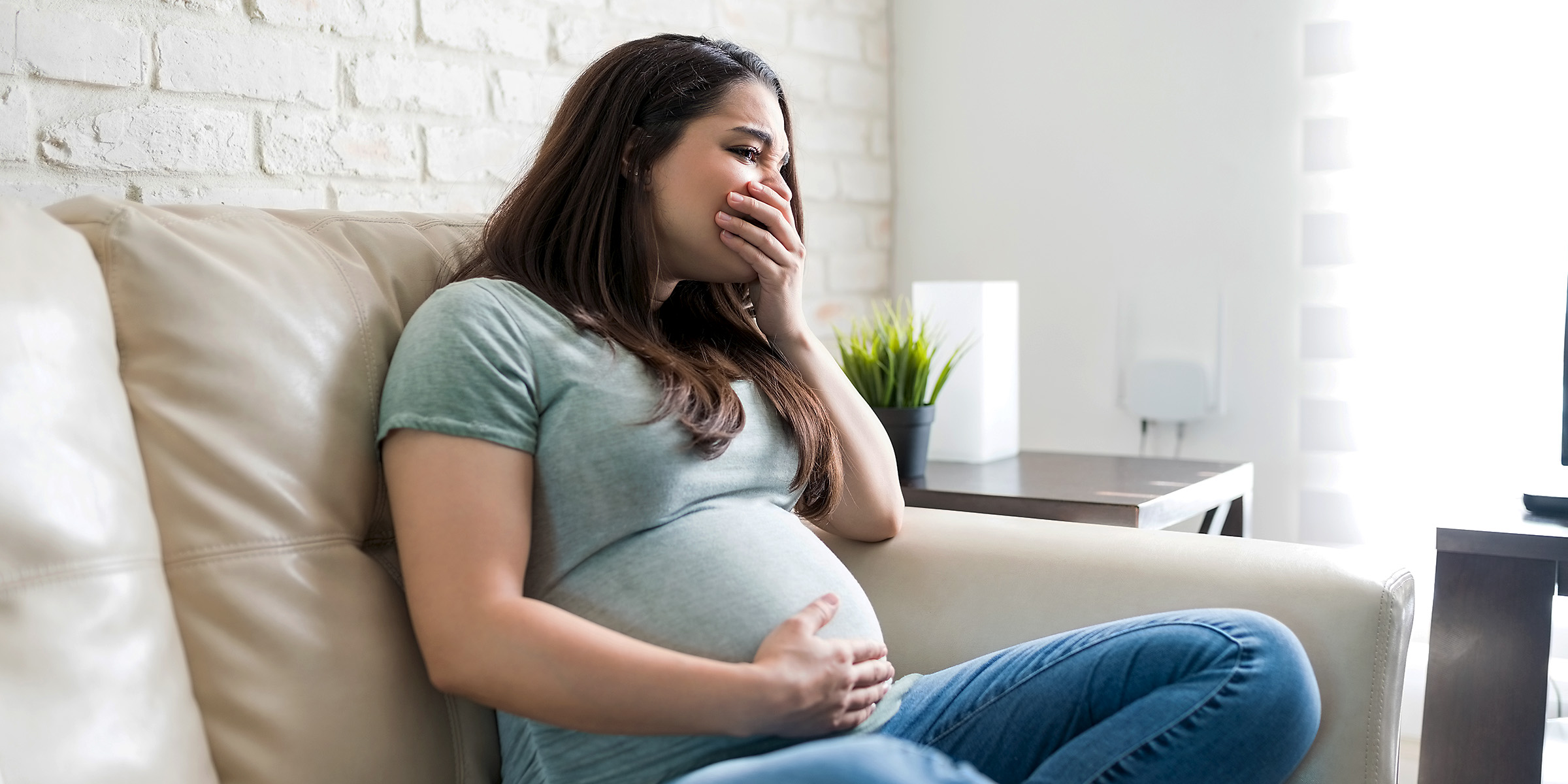 Eine aufgeregte schwangere Frau sitzt auf einer Couch | Quelle: Shutterstock