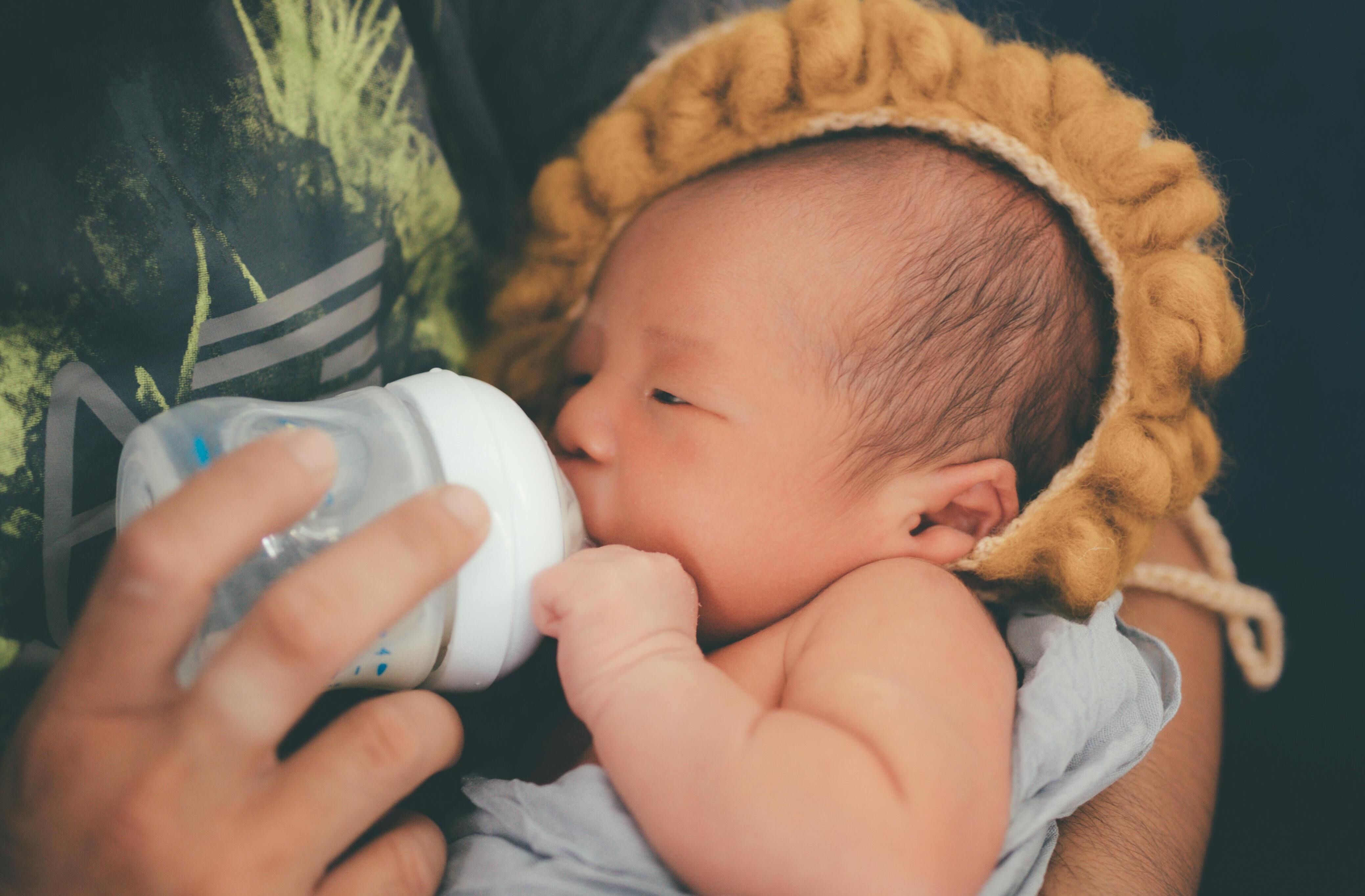 Eine Person, die ein neugeborenes Baby mit der Flasche füttert, während das Baby einen süßen Löwenhut trägt | Quelle: Pexels