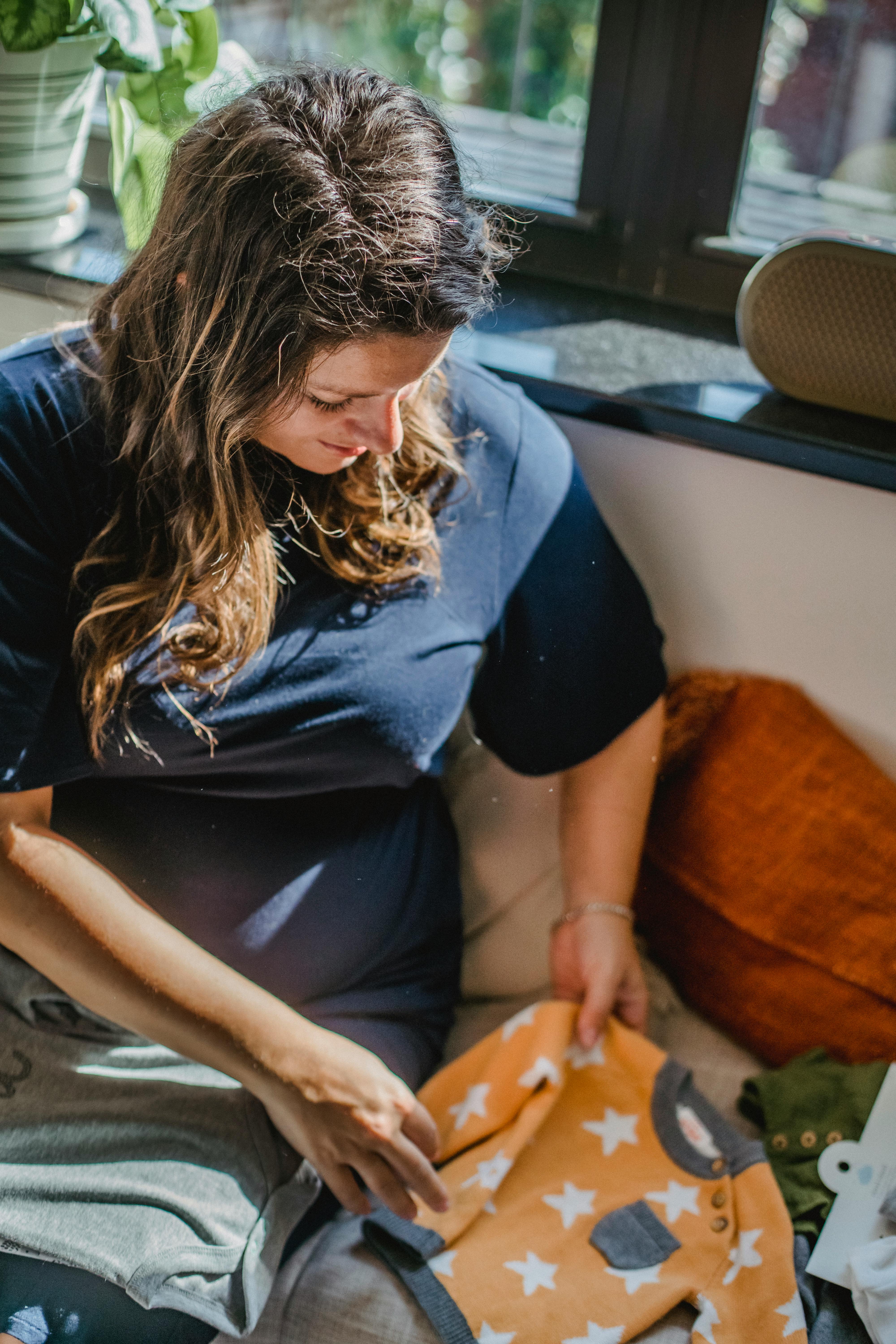 Eine schwangere Frau mit Babykleidung sitzend | Quelle: Pexels