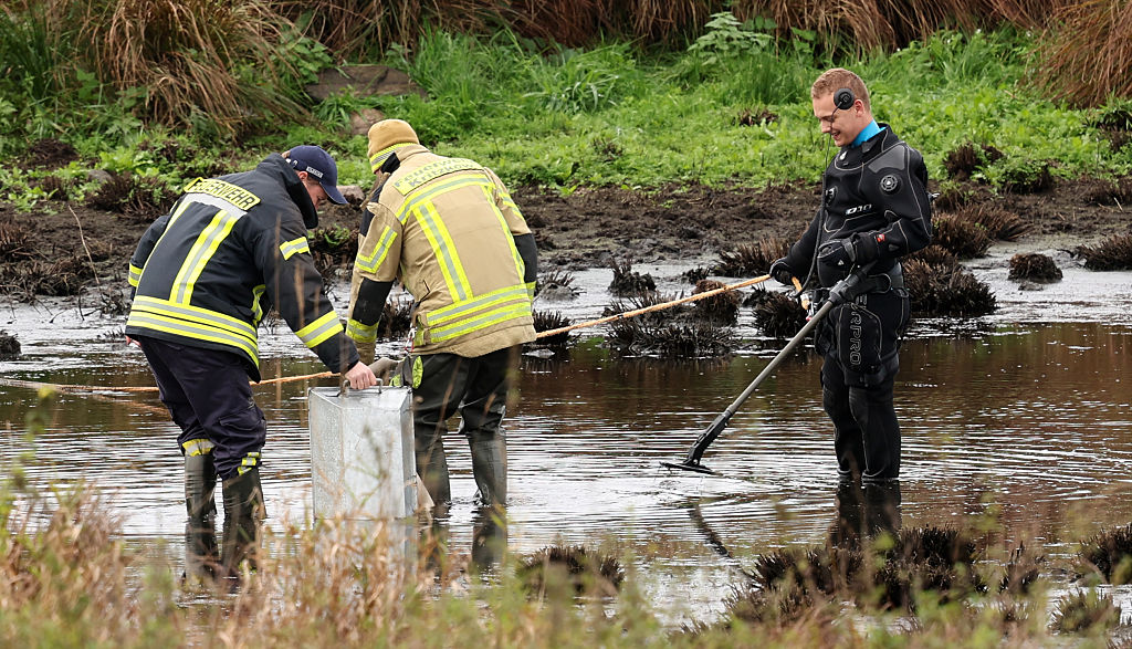 17. Oktober 2025, Mecklenburg-Vorpommern, Klein Upahl: An der Stelle, an der der achtjährige Fabian aus Güstrow tot in einem kleinen Teich bei Klein Upahl gefunden wurde, pumpt die Feuerwehr das Wasser ab, während ein Polizist mit einem Detektor im Einsatz ist. | Quelle: Getty Images