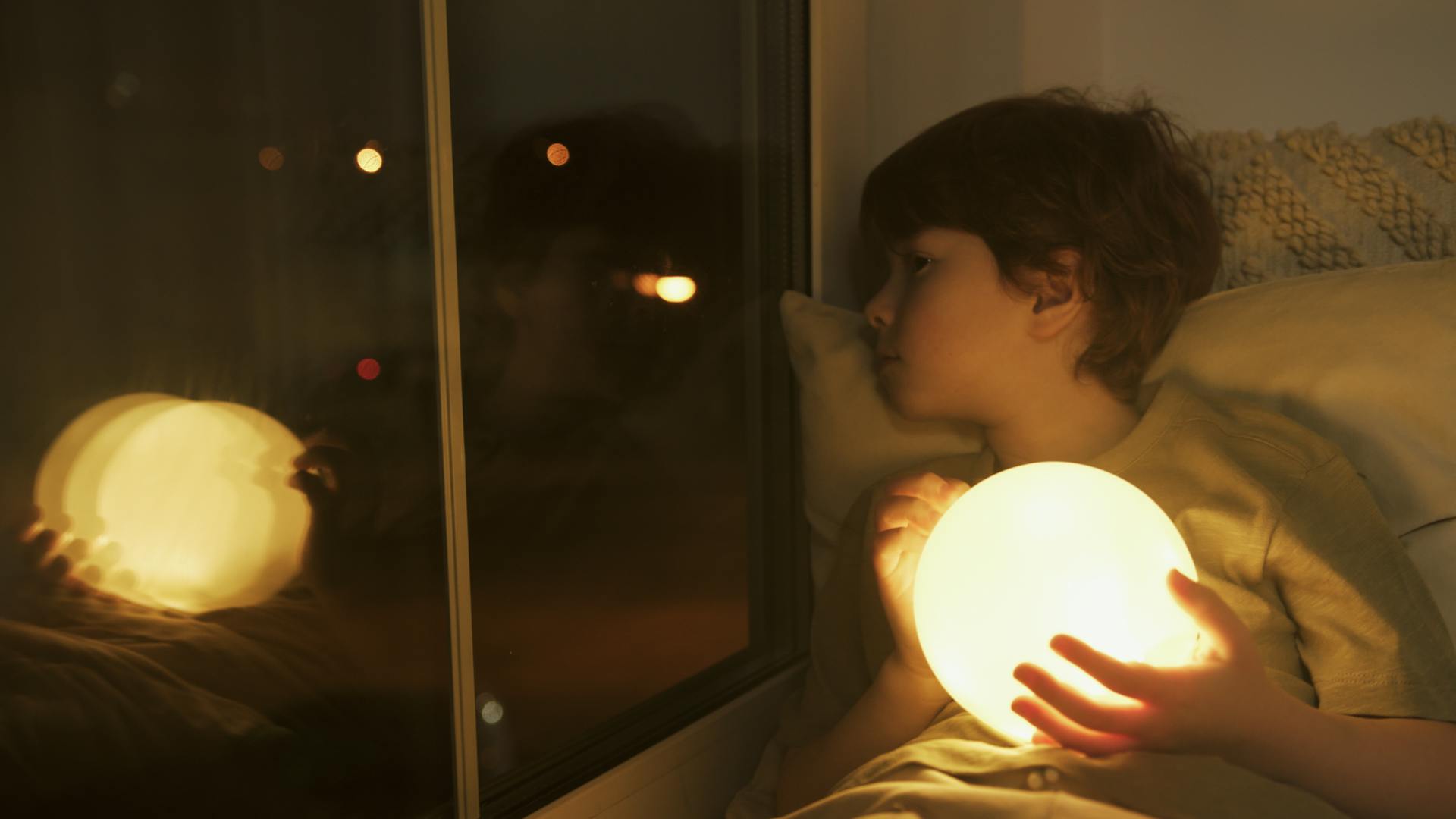 Ein Junge hält eine Lichtkugel und schaut aus dem Fenster | Quelle: Pexels
