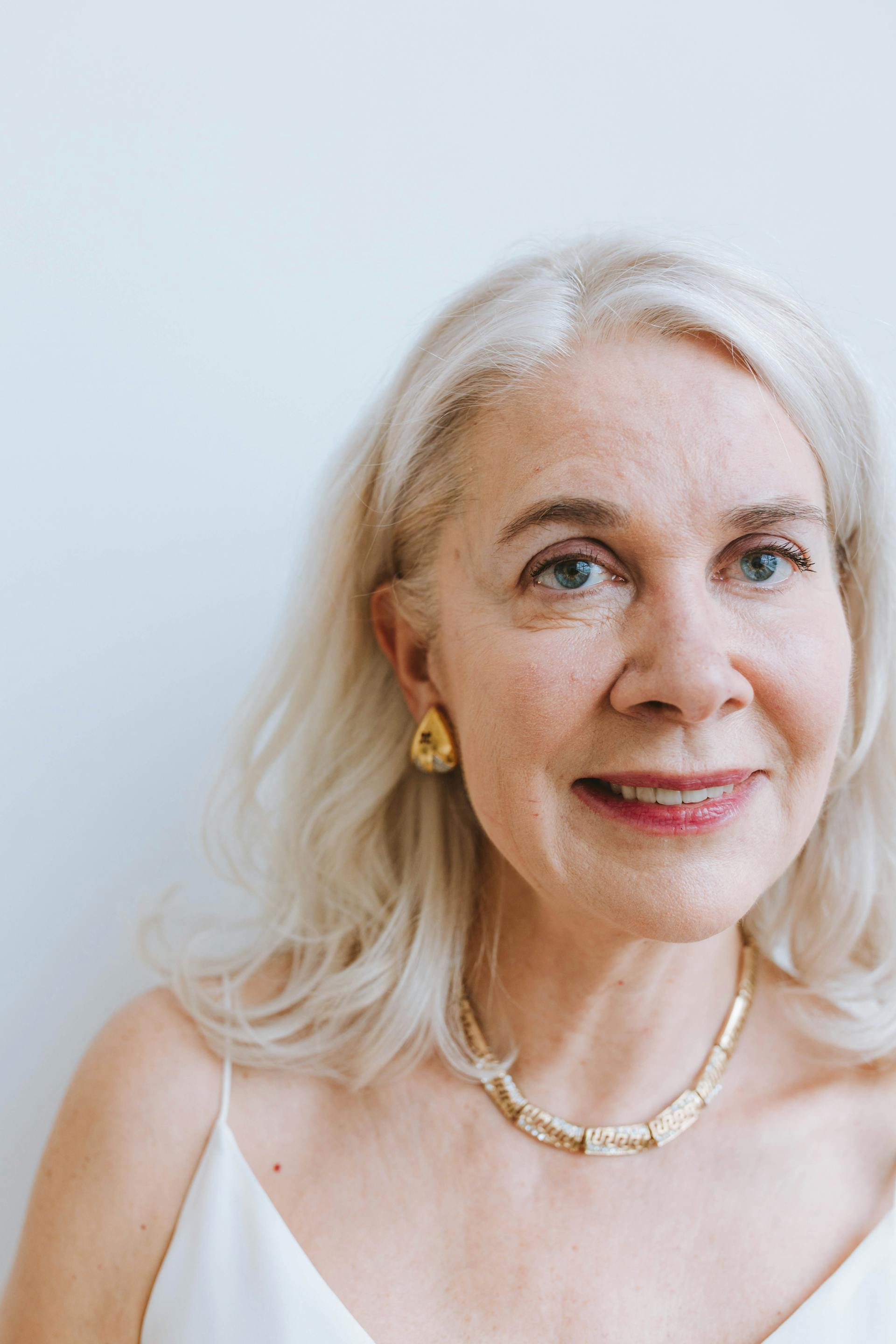 Eine reife Frau mit langen grauen Haaren lächelt, während sie goldene Ohrringe und eine Halskette trägt | Quelle: Pexels