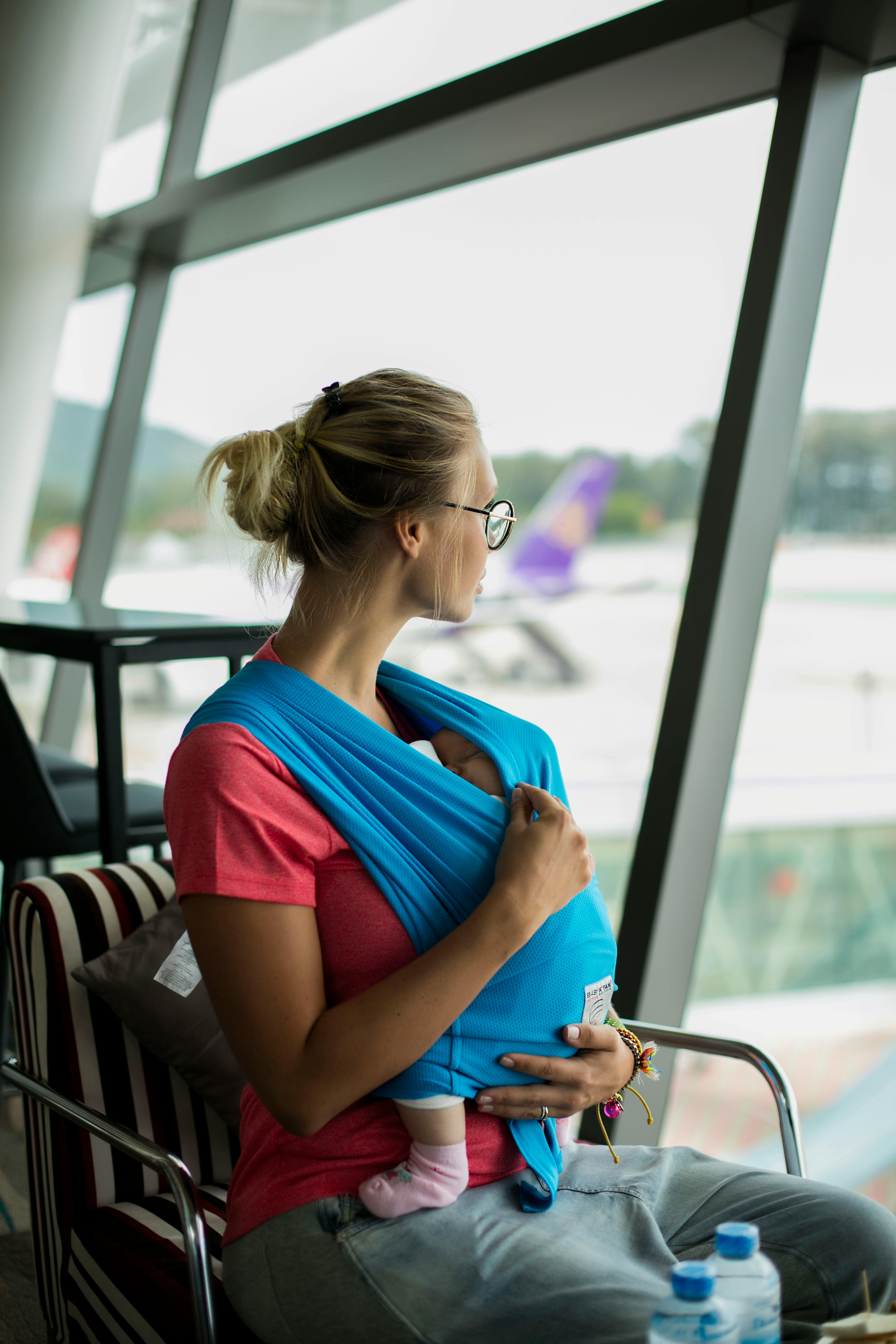 Blonde Frau mit einem Baby, das durch das Fenster eines Flughafens schaut | Quelle: Pexels