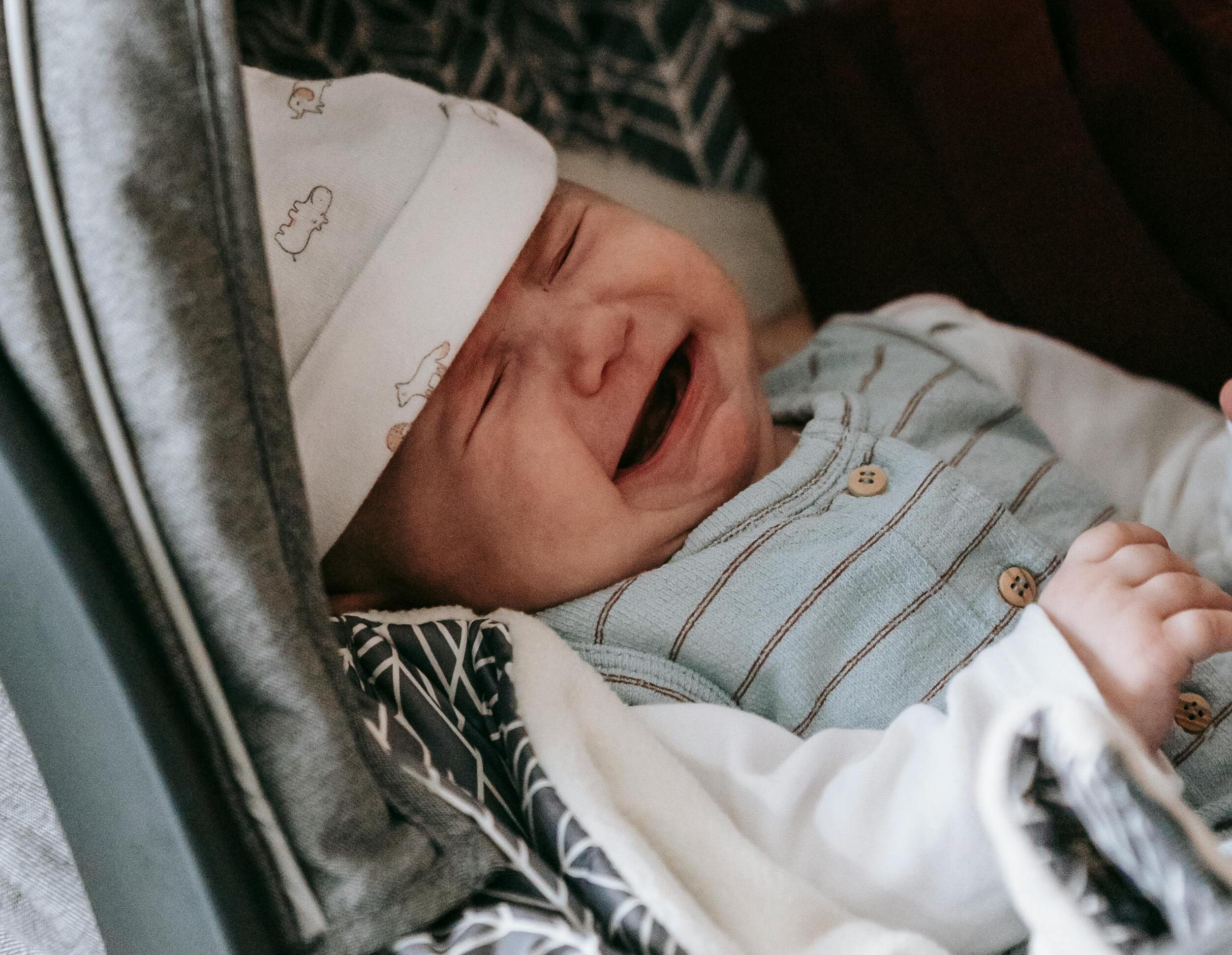 Ein Baby in einem gestreiften Strampler und einer weißen Mütze, das weint | Quelle: Pexels