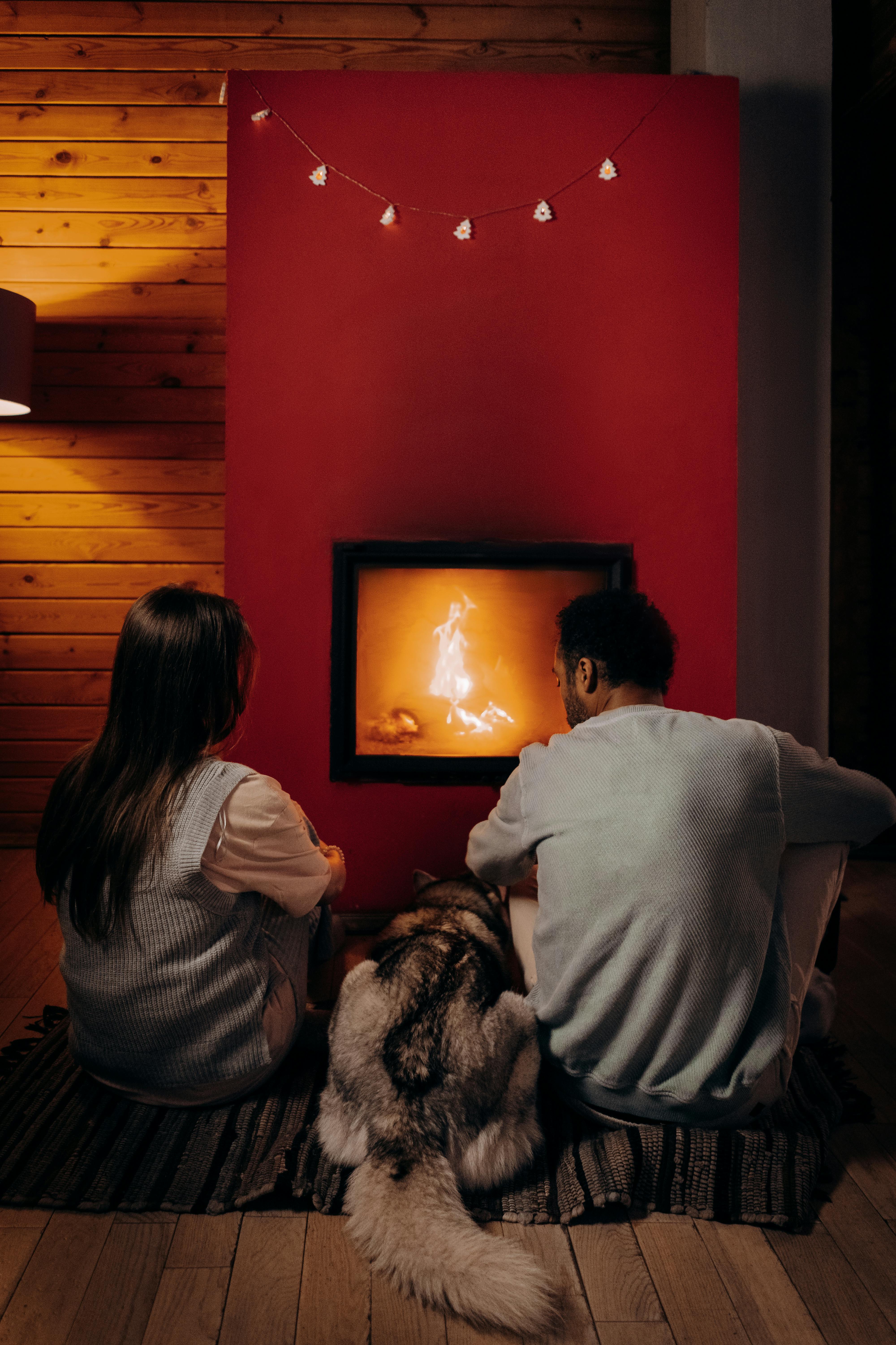 Ein Paar sitzt mit seinem Hund vor einem Kamin | Quelle: Pexels
