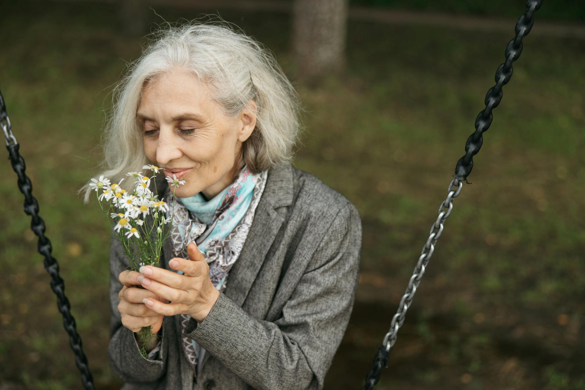 Ältere Frau sitzt auf einer Schaukel und riecht an Blumen | Quelle: Pexels