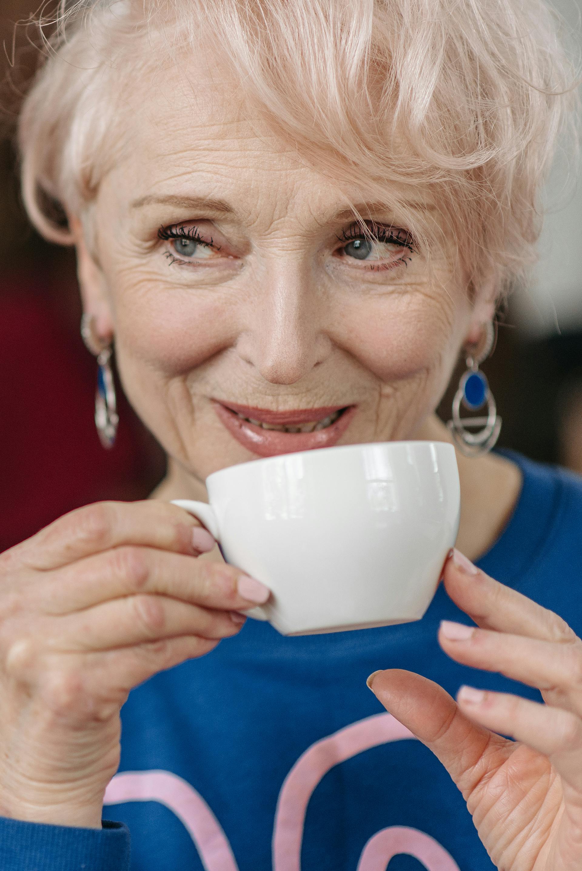 Eine lächelnde Seniorin, die ihren Kaffee trinkt und dabei jemanden ansieht | Quelle: Pexels
