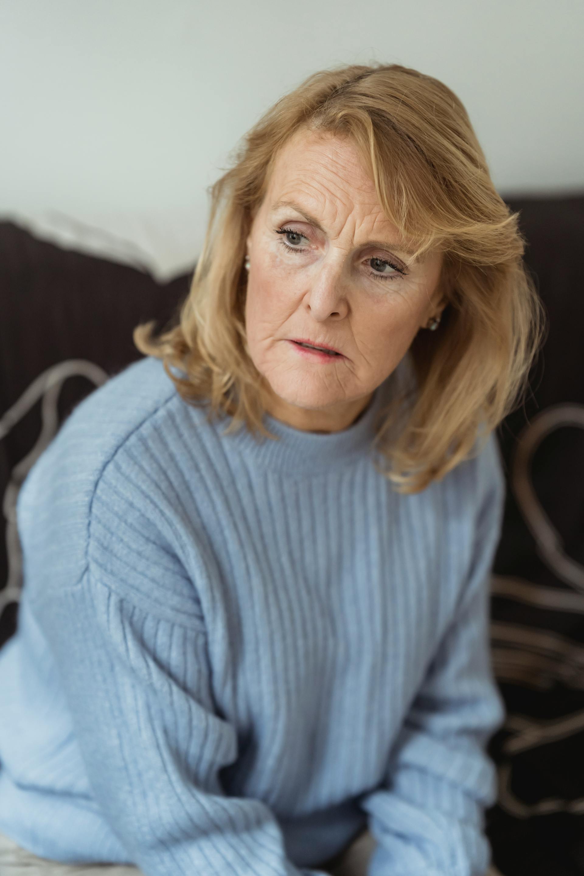 Eine aufgebrachte ältere Frau, die auf einer Couch sitzt | Quelle: Pexels