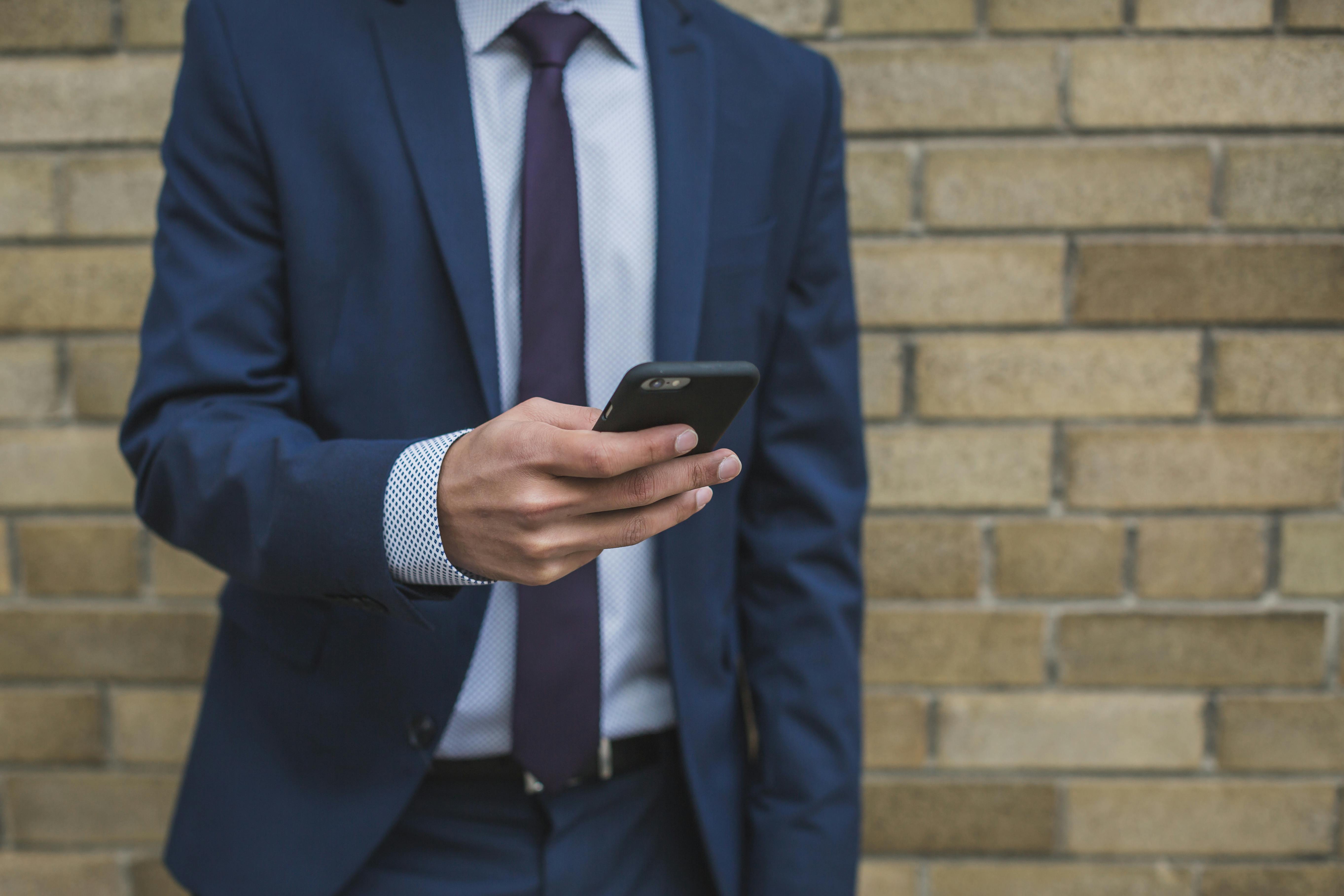 Mann im Anzug benutzt sein Smartphone | Quelle: Pexels