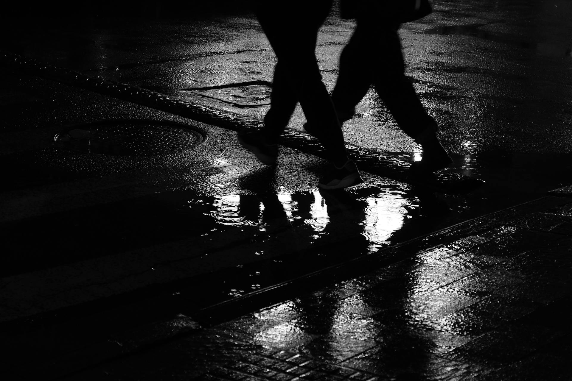 Silhouette von zwei Männern, die auf einer nassen Straße gehen | Quelle: Pexels