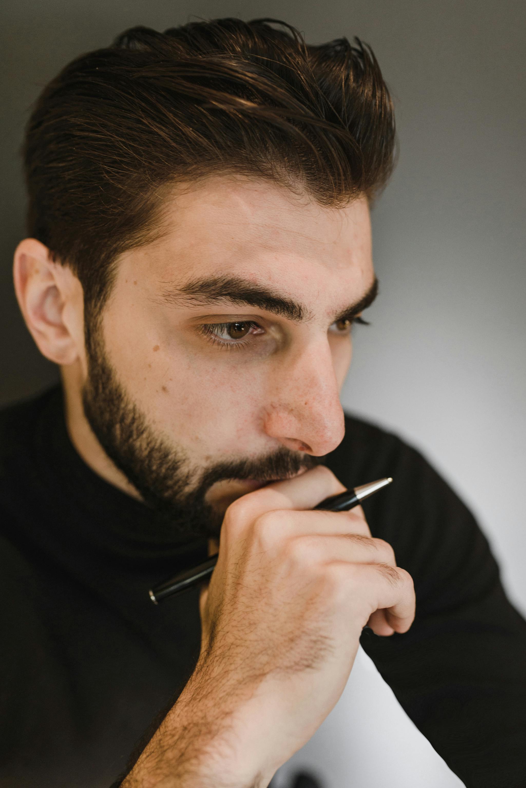 Mann hält einen Stift und denkt nach | Quelle: Pexels