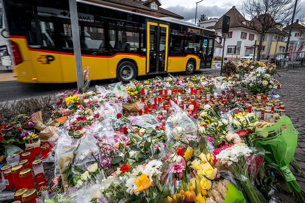 Ein PostAuto fährt an Blumen und Kerzen vorbei an der Stelle, an der ein Bus desselben Verkehrsunternehmens in Flammen aufgegangen war | Quelle: Getty Images