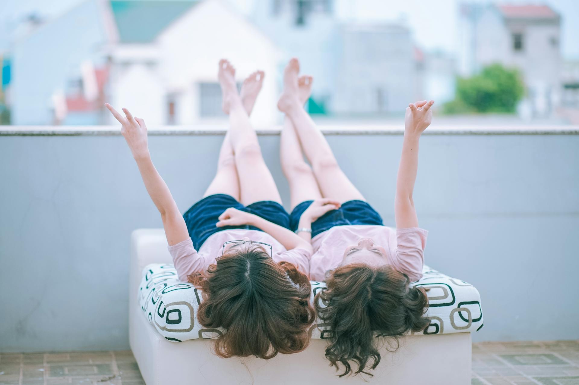 Zwei junge Frauen, die auf einem Balkon liegen und Friedenszeichen blinken | Quelle: Pexels