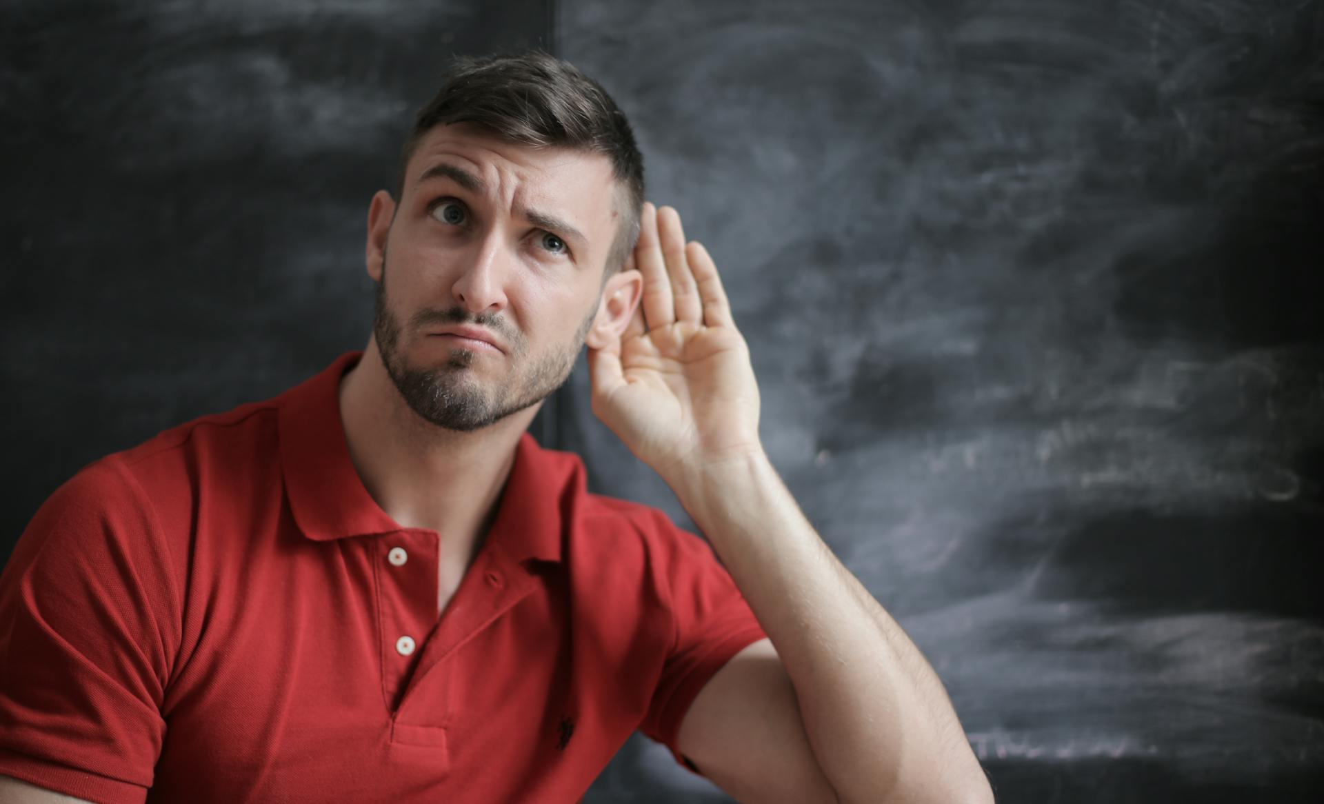 Ein Mann, der seine Hand hinter sein Ohr legt | Quelle: Pexels