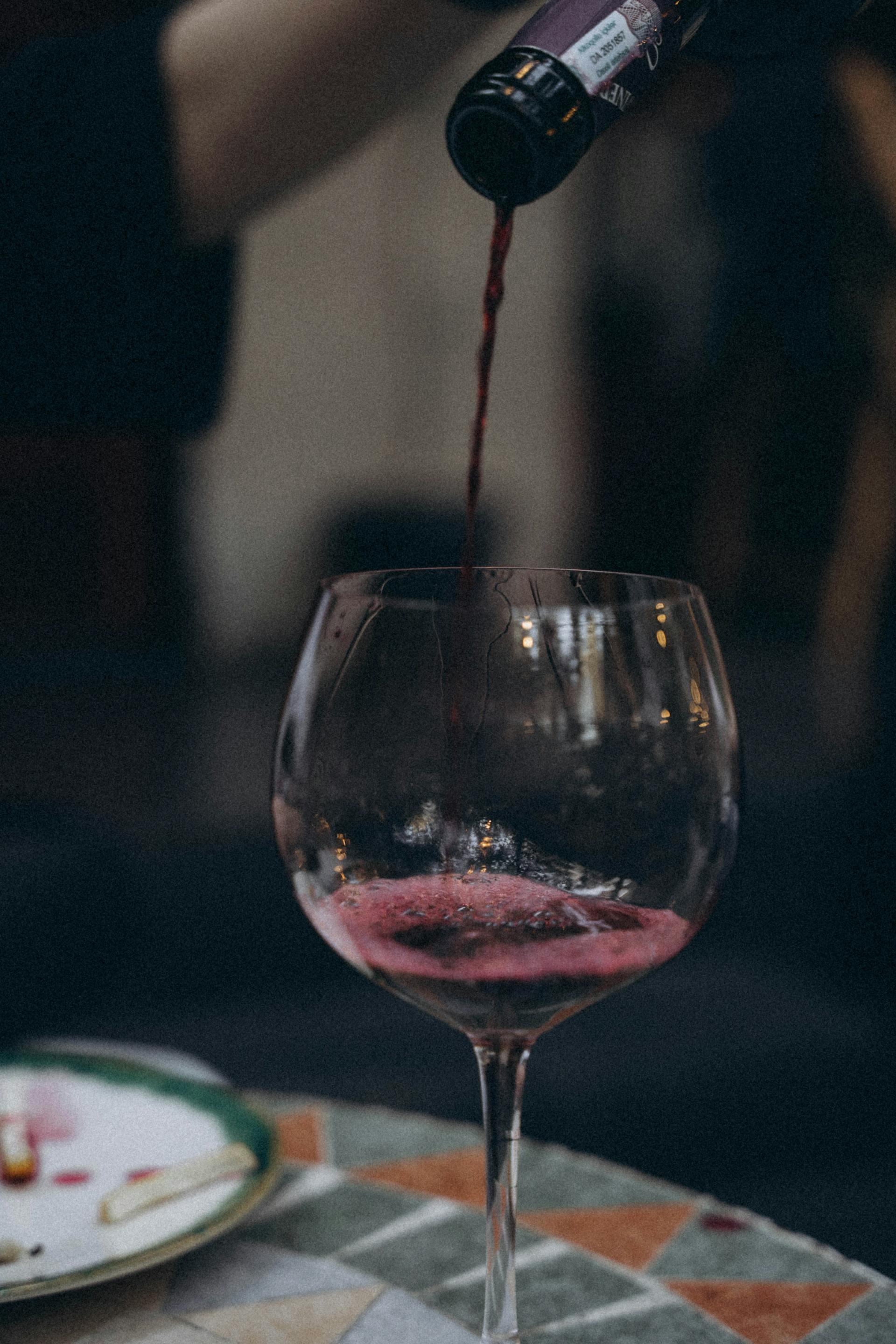 Eine Nahaufnahme von einer Person, die Rotwein in ein Glas gießt | Quelle: Pexels