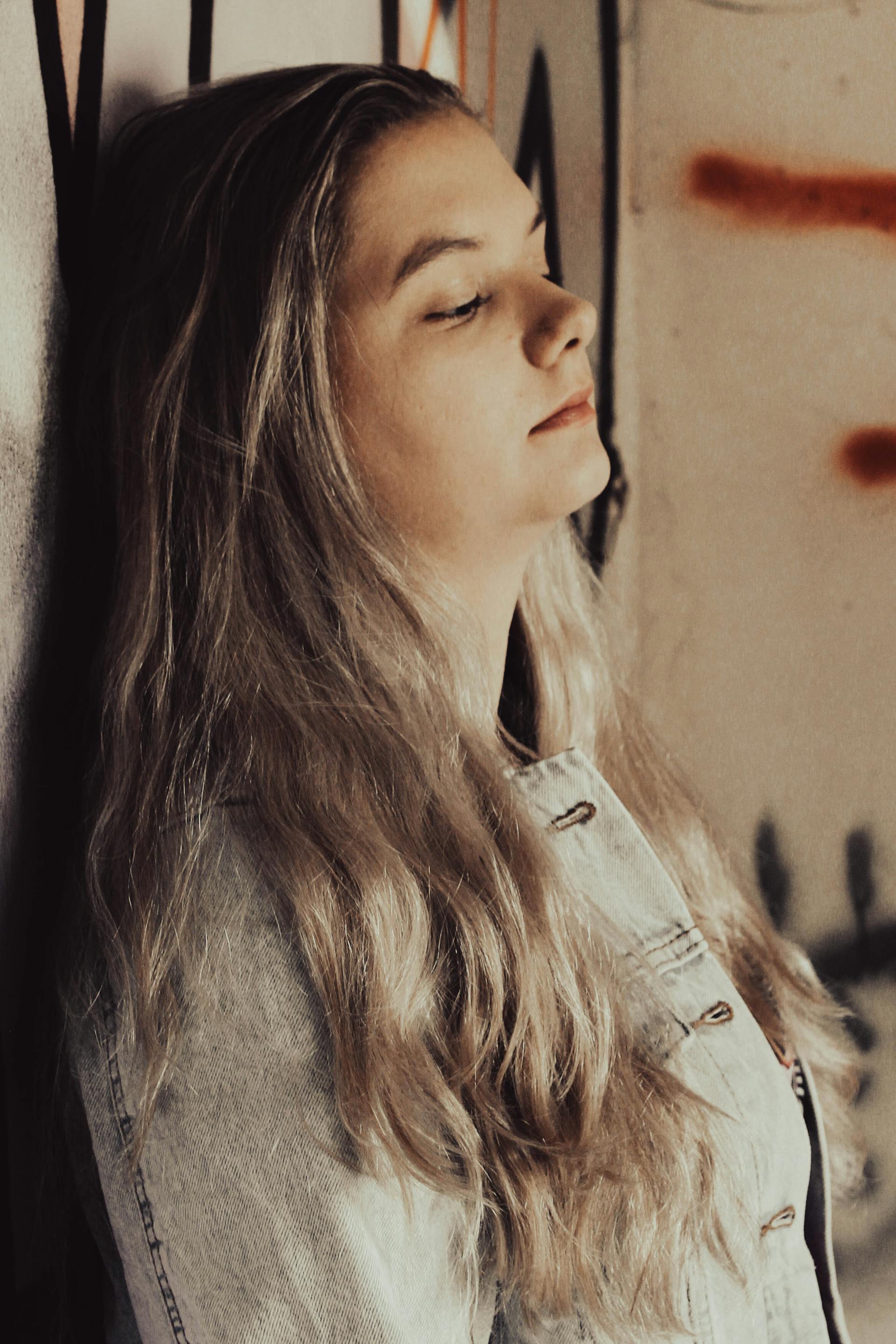 Eine traurige Frau in Jeansjacke mit geschlossenen Augen, die an einer Wand lehnt | Quelle: Pexels