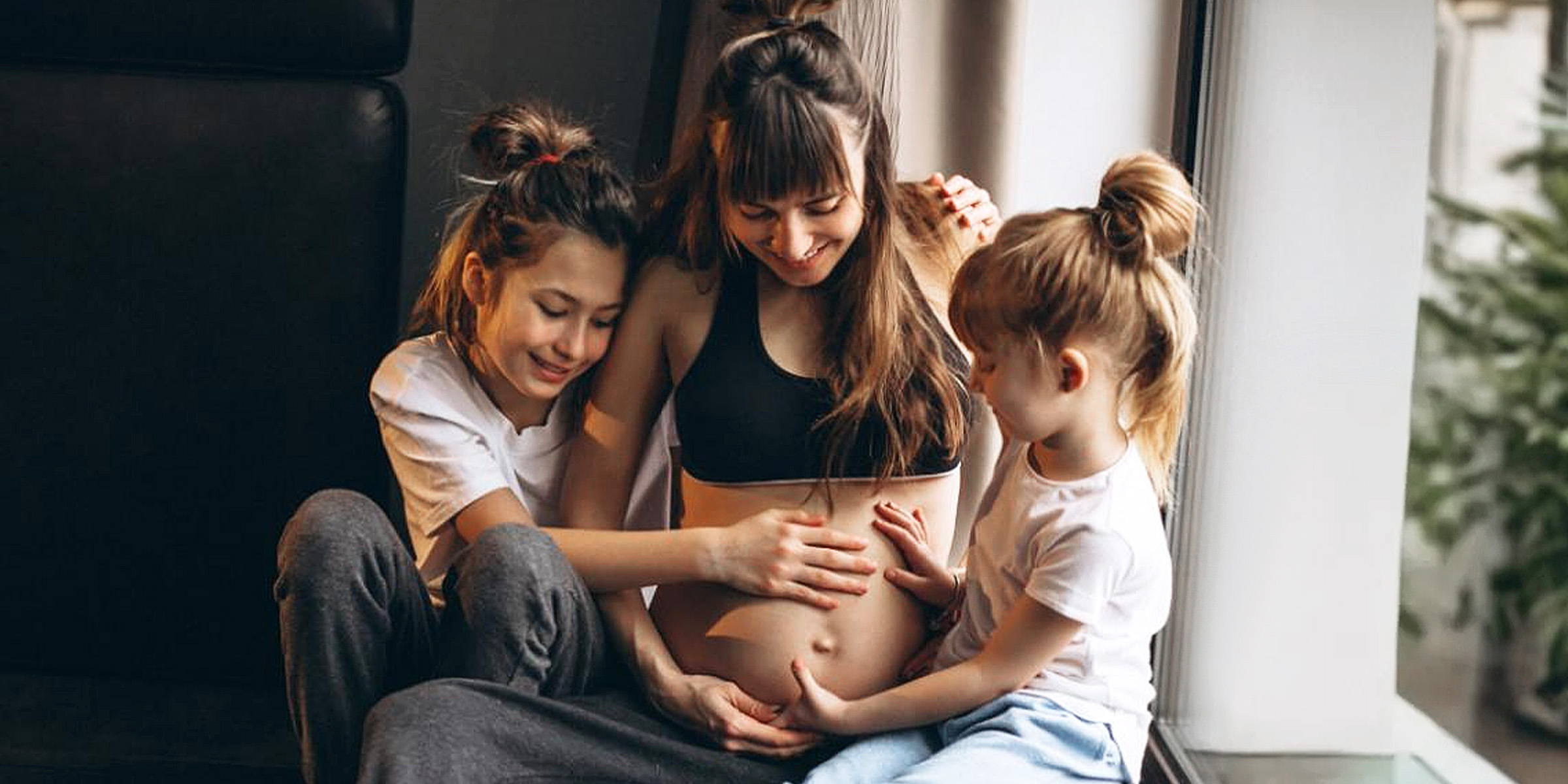 Eine schwangere Frau mit Kindern sitzt am Fenster | Quelle: Freepik