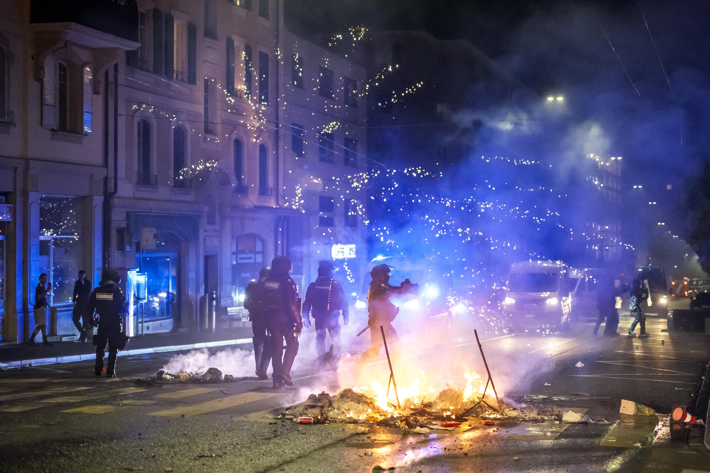 Feuerwerkskörper explodieren in der Nähe von Polizisten in Kampfausrüstung in Lausanne am 25. August 2025, in der zweiten Nacht der Proteste nach dem Tod eines Teenagers, der mit einem gestohlenen Motorroller vor der örtlichen Polizei fliehen wollte. | Quelle: Getty Images