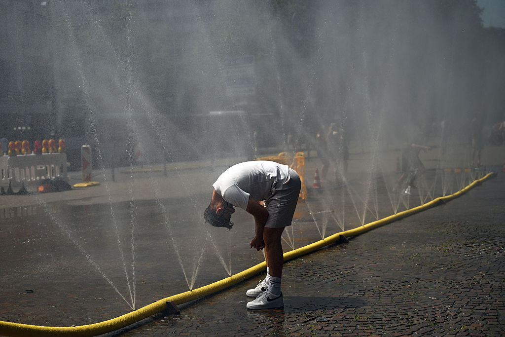 Ein Mann kühlt seinen Kopf an Wasserschläuchen, aus denen Wasser spritzt, um Abkühlung von der Sommerhitze zu bieten – dies ist Teil der Klimaanpassungsmaßnahmen in Köln, Westdeutschland, am 25. Juni 2026 während einer Hitzewelle in Europa. | Quelle: Getty Images