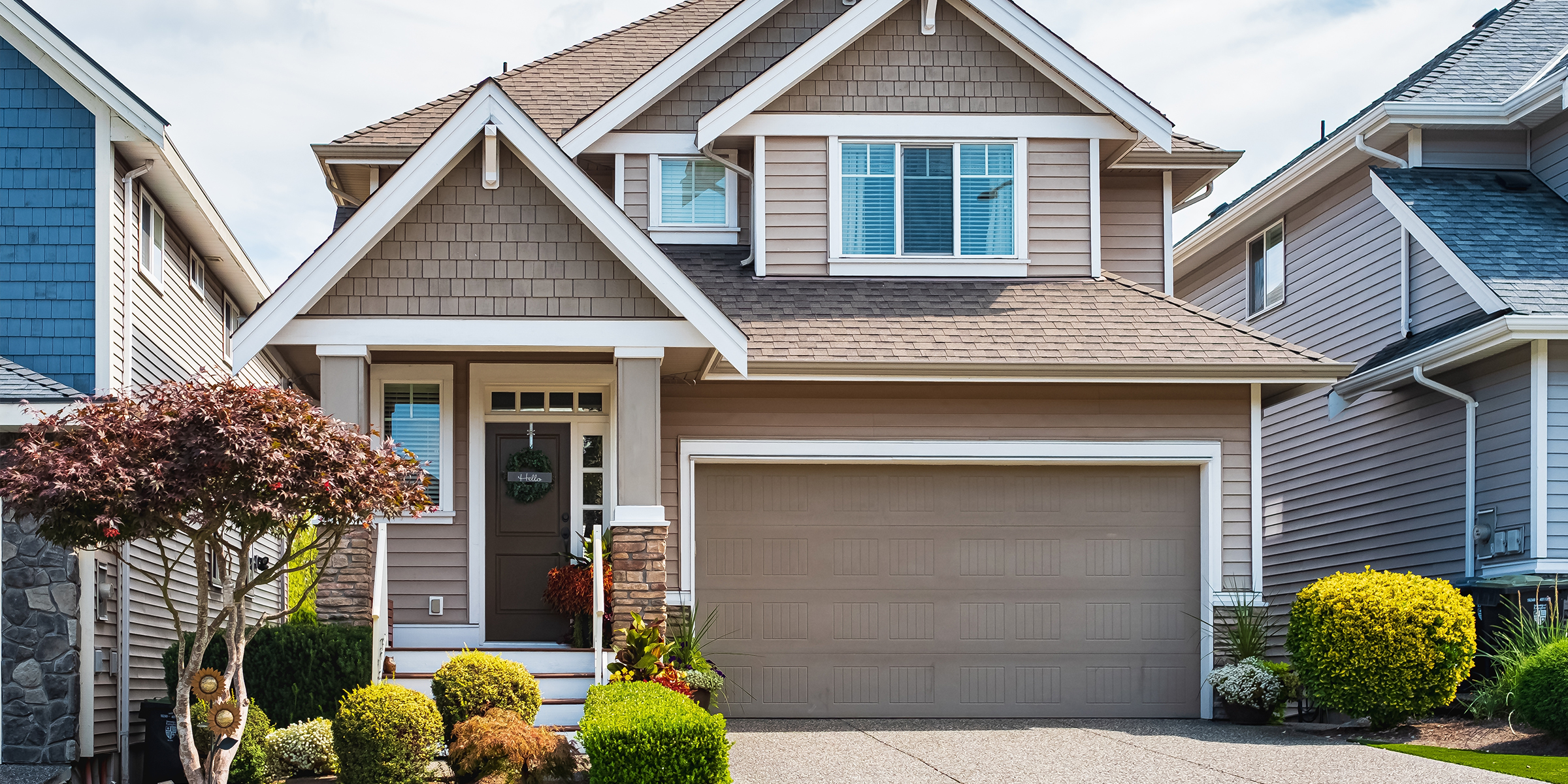 Ein modernes Vorstadthaus mit einem gepflegten Garten, beigen Seitenwänden und einer Garage | Quelle: Shutterstock