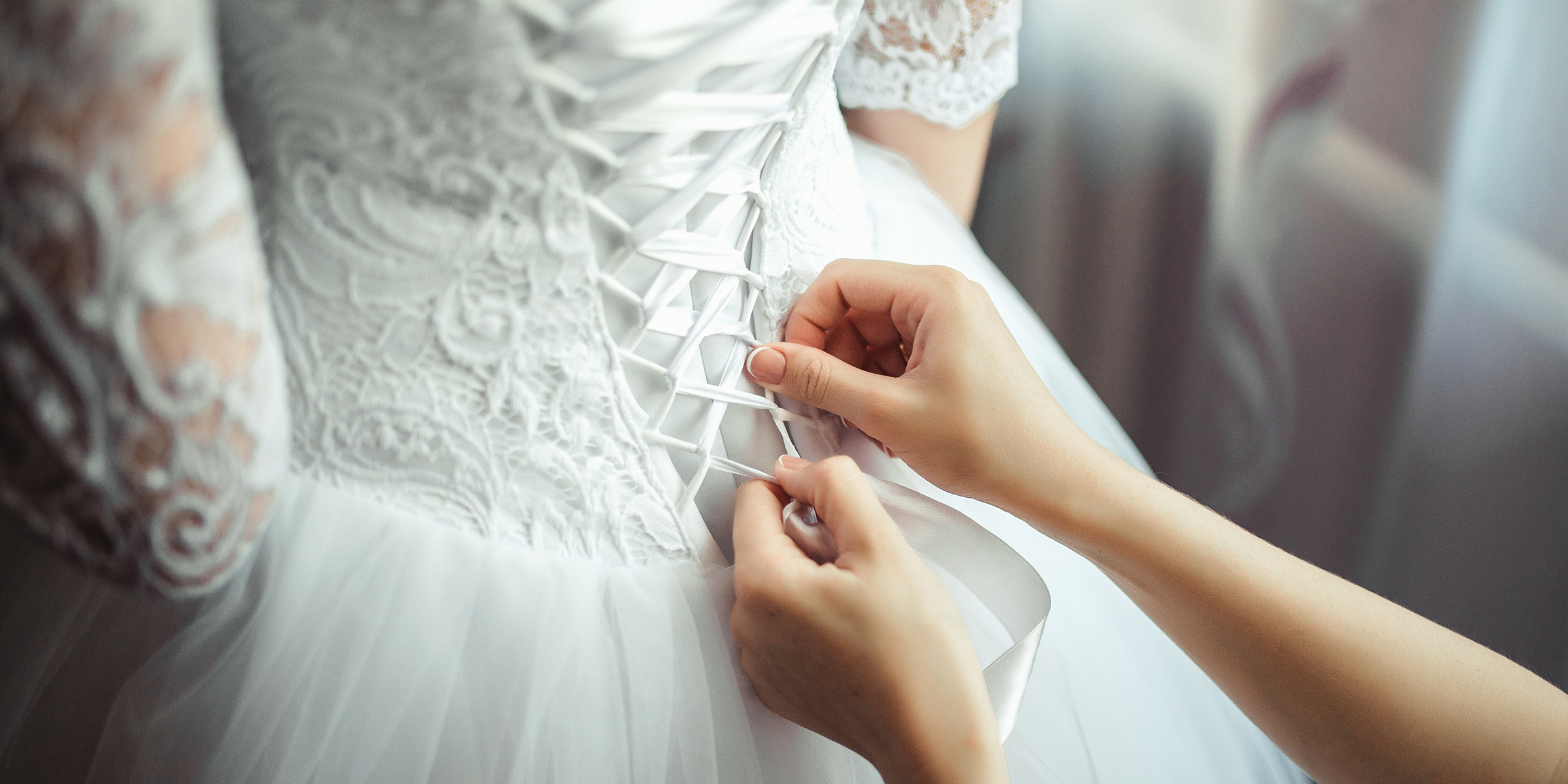 Eine Brautjungfer macht einen Knoten in das Kleid der Braut | Quelle: Shutterstock