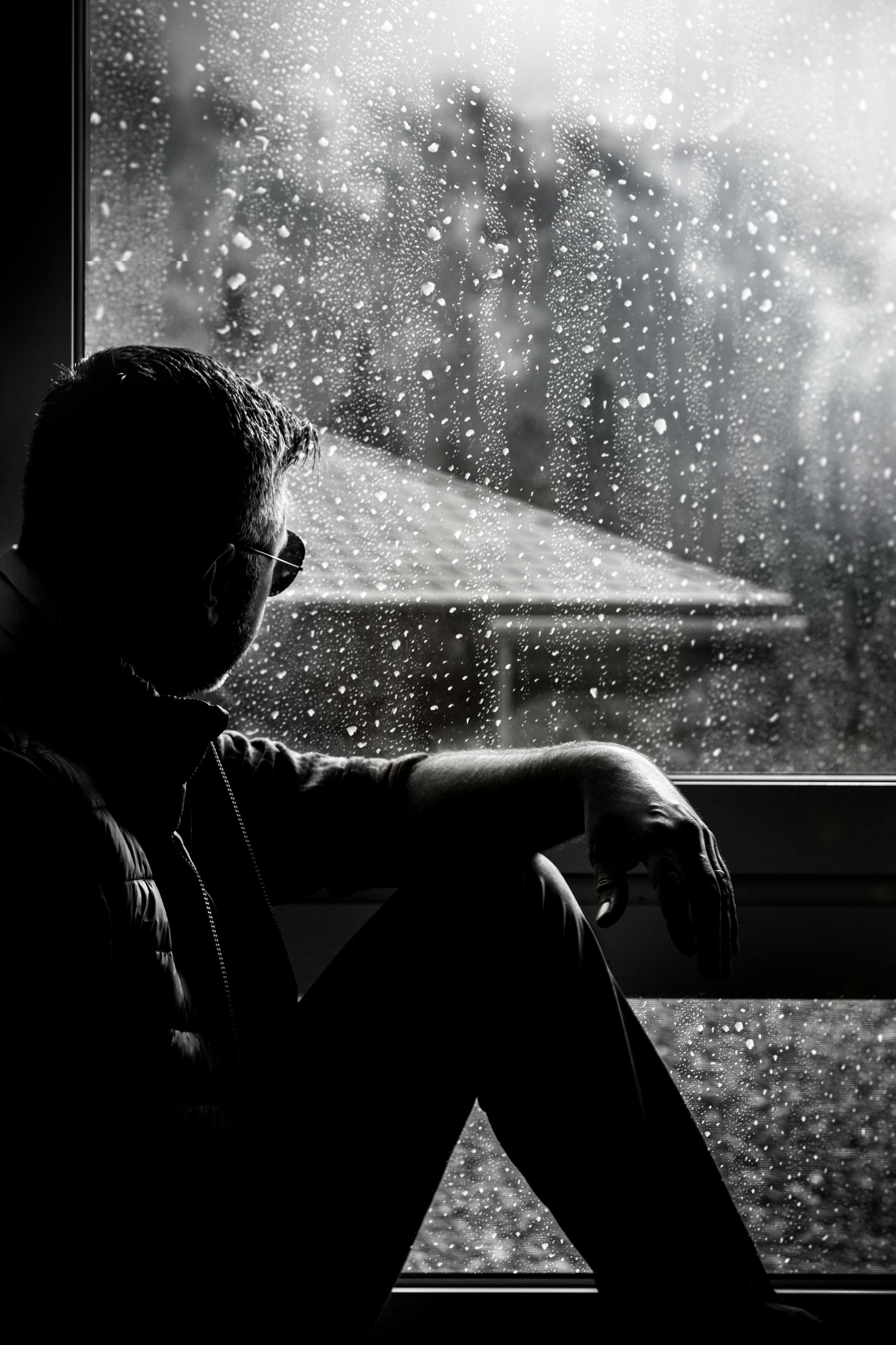 Ein Schwarz-Weiß-Foto eines Mannes, der neben einem Fenster sitzt | Quelle: Pexels