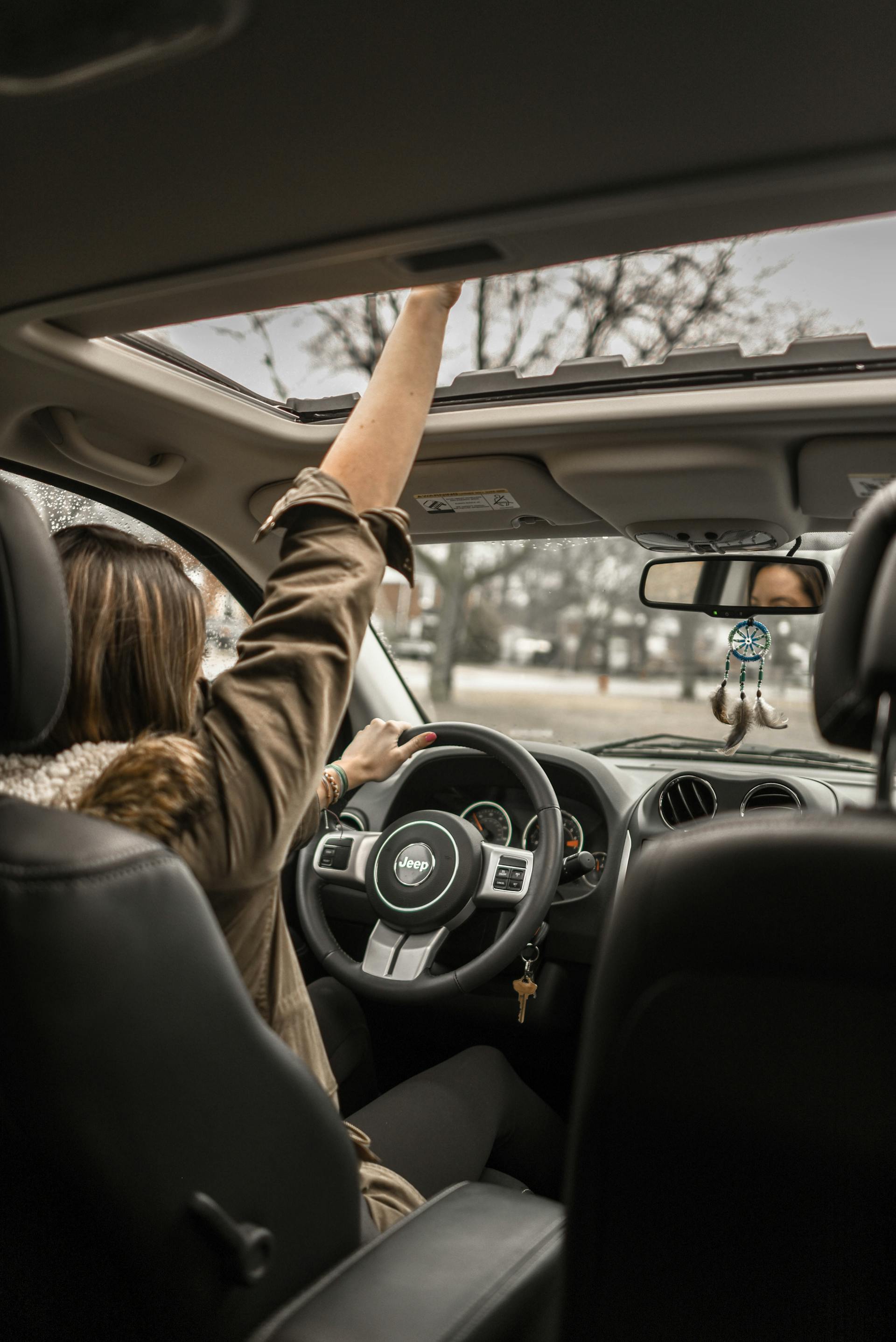 Eine Frau winkt durch ein offenes Schiebedach in einem Auto | Quelle: Pexels