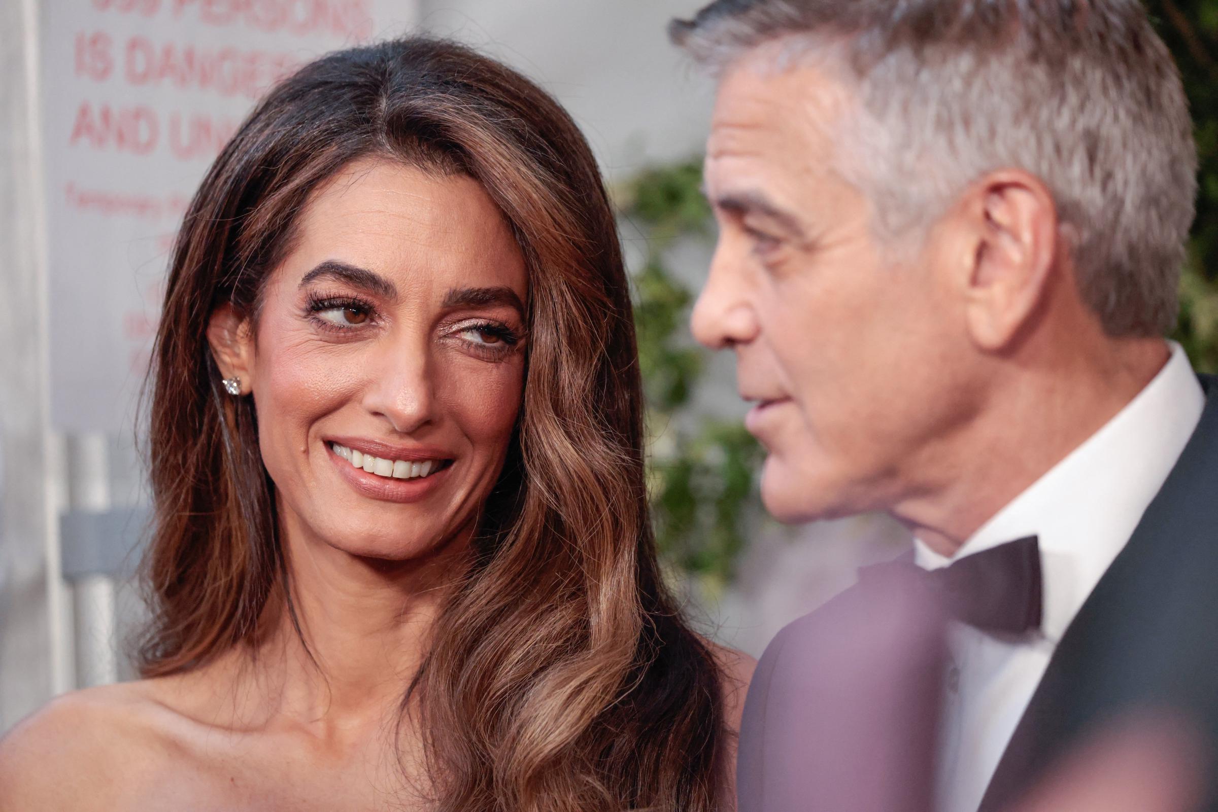 Amal Clooney sieht George mit einem sanften Lächeln an, ihr Ausdruck ist warm und entspannt. Die Nahaufnahme fängt einen ruhigen Moment zwischen dem Paar auf dem roten Teppich ein.