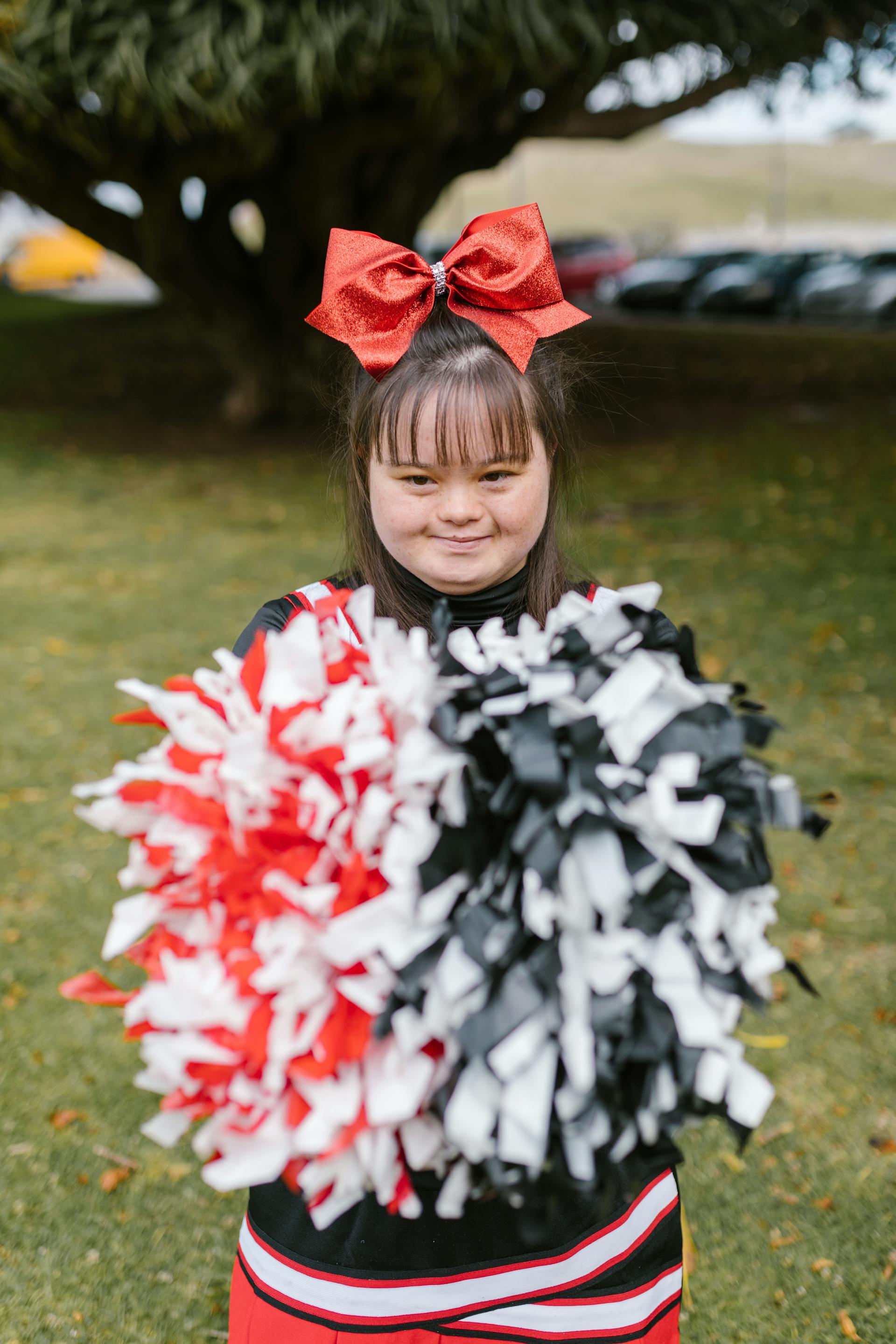 Ein junges Mädchen mit Down-Syndrom in einem Cheerleader-Outfit und mit Pompons in der Hand | Quelle: Pexels