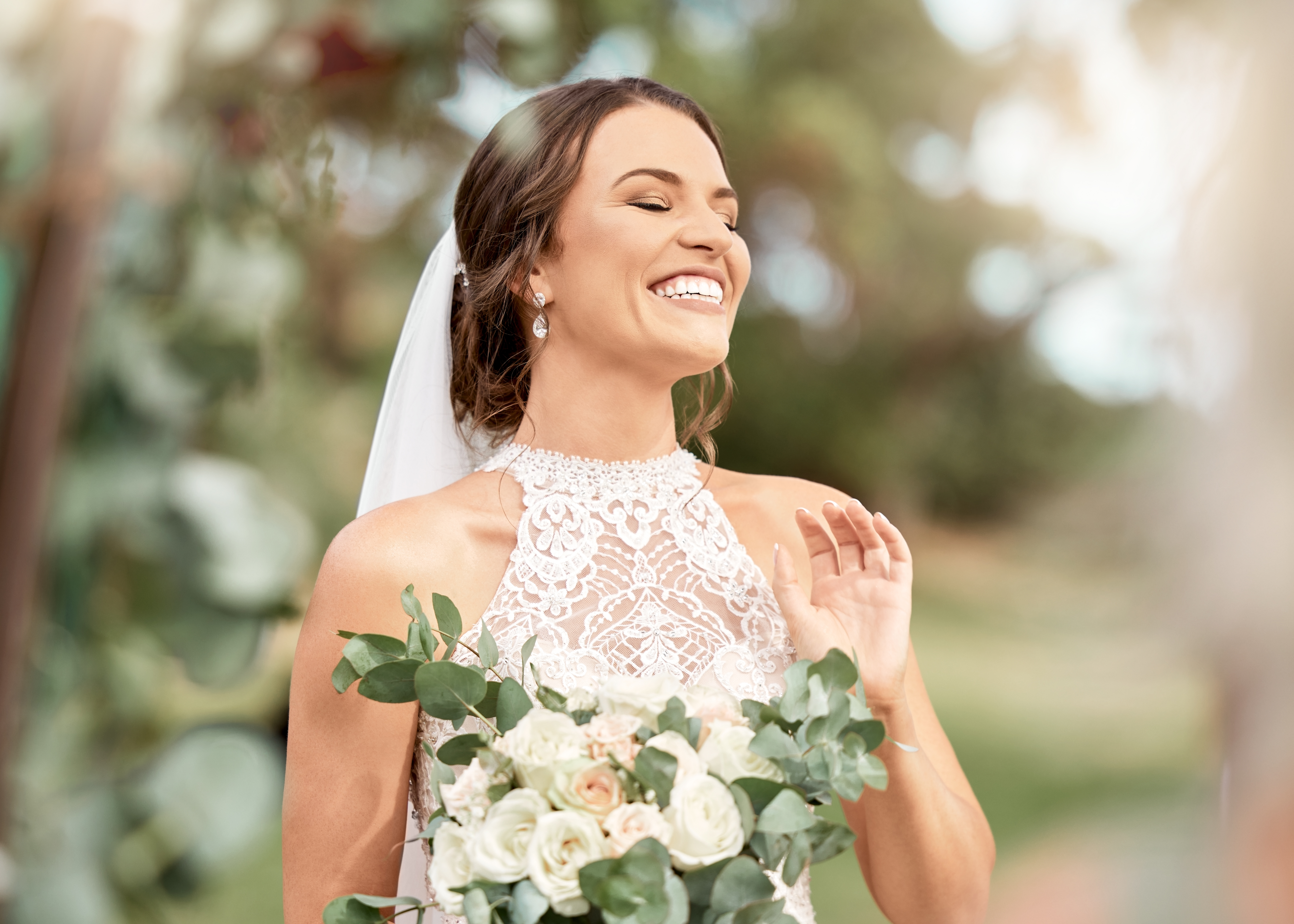 Aufgeregte Braut bei der Hochzeit mit Blumenstrauß im Naturpark mit grünen Bäumen, Bokeh und Sommersonne. Glück, Engagement und Traum einer schönen Frau mit Blumen für die Hochzeit im Freien Lens Flare | Quelle: Getty Images