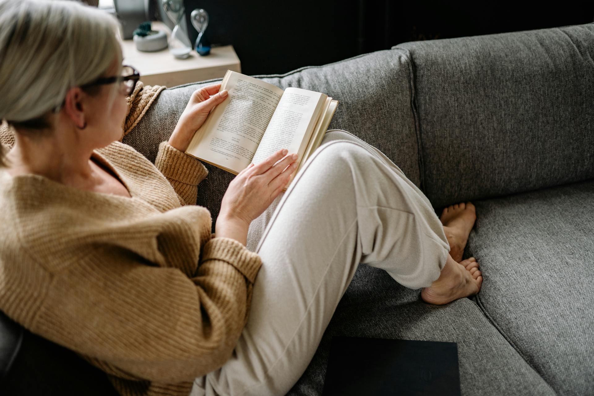 Eine ältere Frau liest ein Buch, während sie auf einem Sofa sitzt | Quelle: Pexels