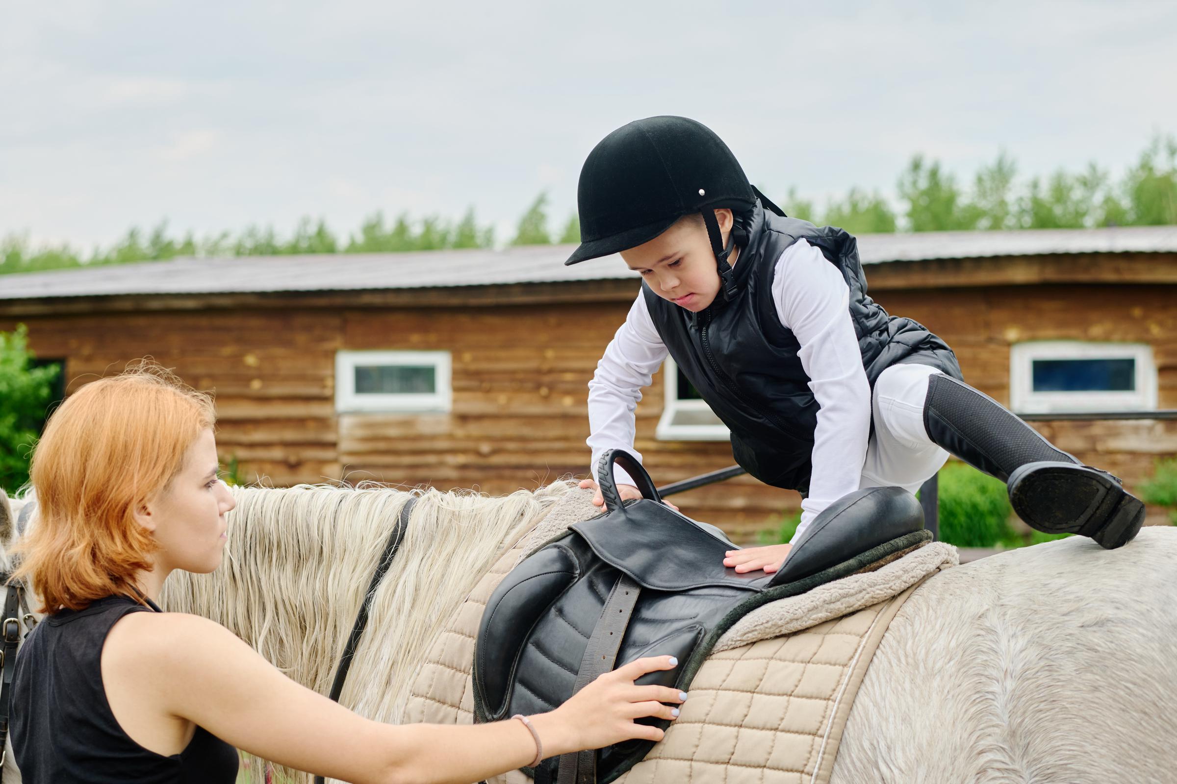 Ein Kind steigt auf ein Pferd, das ein Reitpad trägt – eine Art leichter, baumloser Sattel, meistens mit einer Befestigungsmöglichkeit für Steigbügel. (Symbolbild) | Quelle: Getty Images