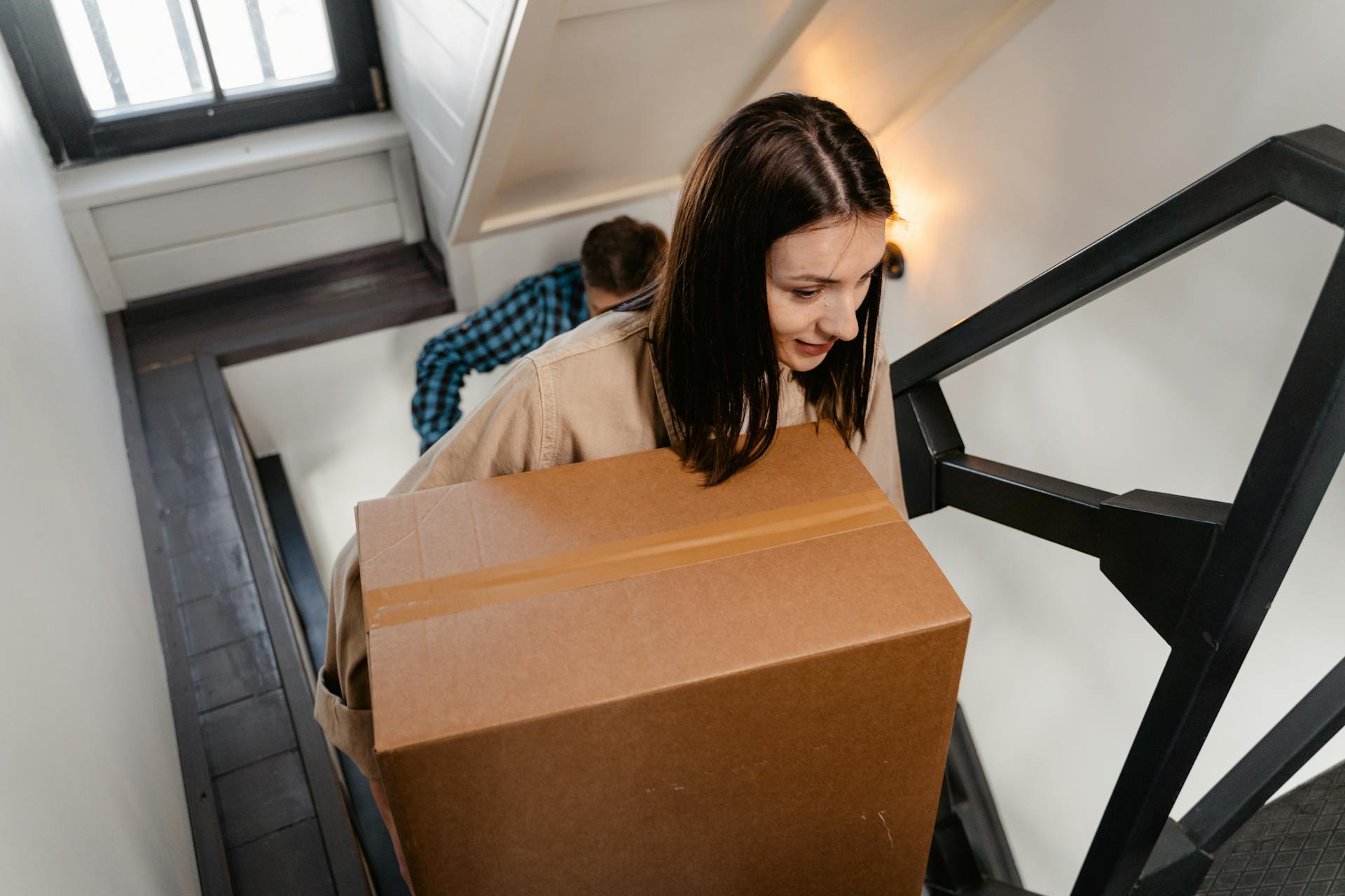 Eine Frau trägt eine Kiste, während sie die Treppe ihres Hauses hinaufsteigt | Quelle: Pexels