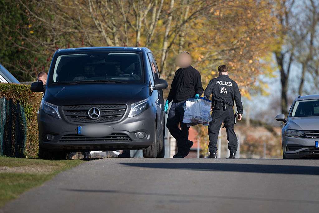 06. November 2025, Mecklenburg-Vorpommern, Güstrow: Ein Ermittler überquert während einer Hausdurchsuchung in Reimershagen die Straße mit Plastiktüten, in denen Sportschuhe stecken | Quelle: Getty Images