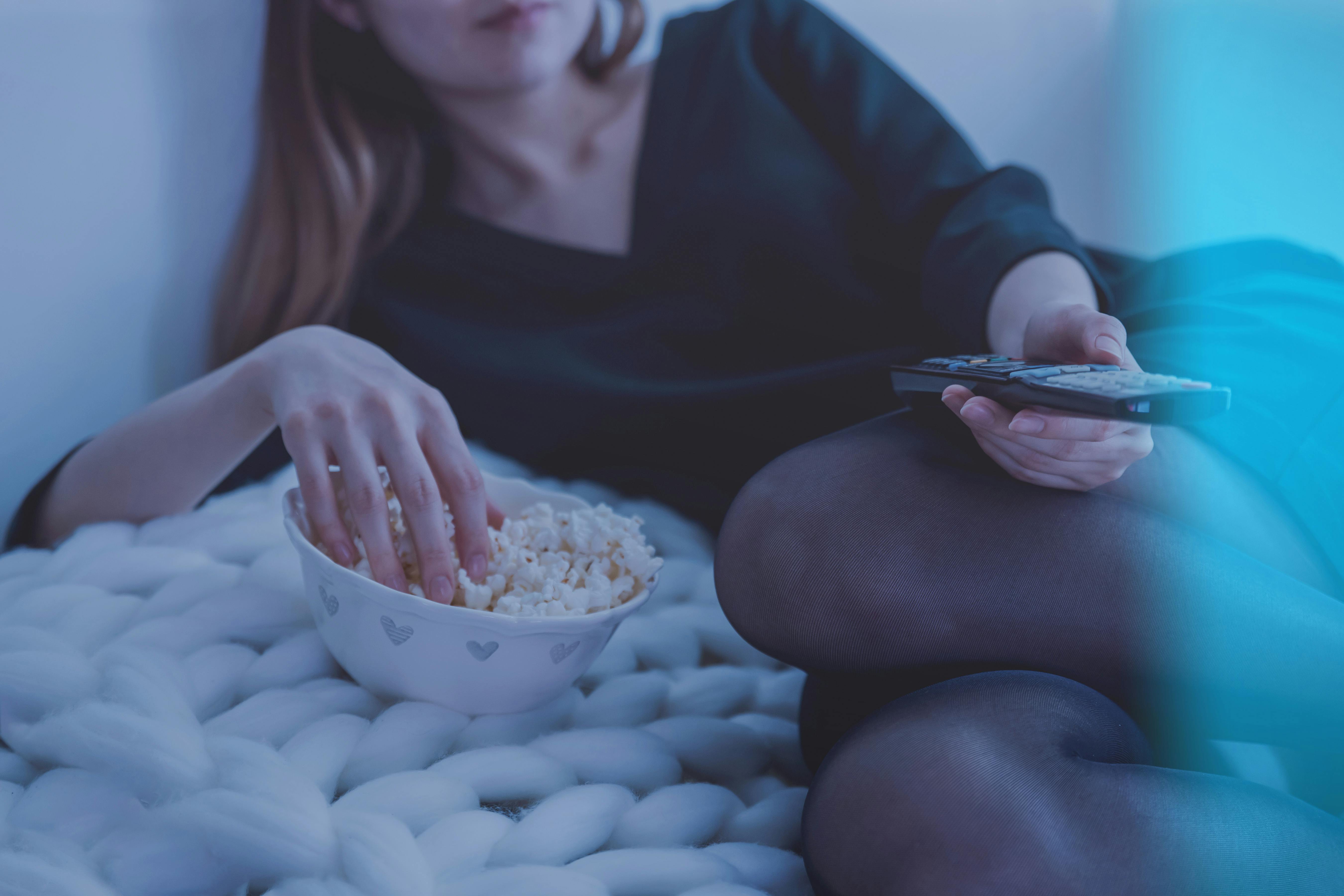 Eine Frau, die eine Schüssel Popcorn isst und eine Fernsehfernbedienung in der Hand hält | Quelle: Pexels