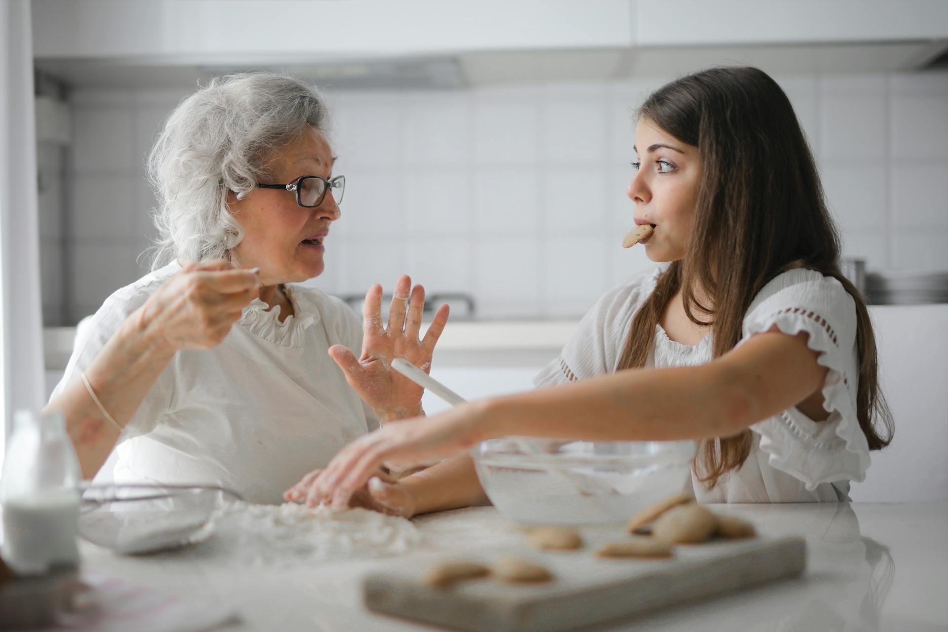 Eine ältere Frau beim Backen mit einem Teenager, der einen Keks mopst | Quelle: Pexels
