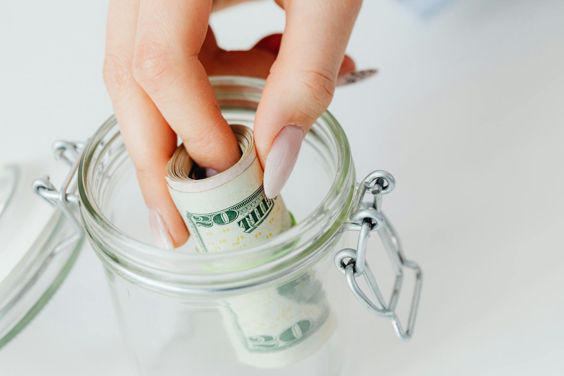 Eine Frau nimmt eine Rolle Dollarnoten aus einem Glasgefäß | Quelle: Pexels