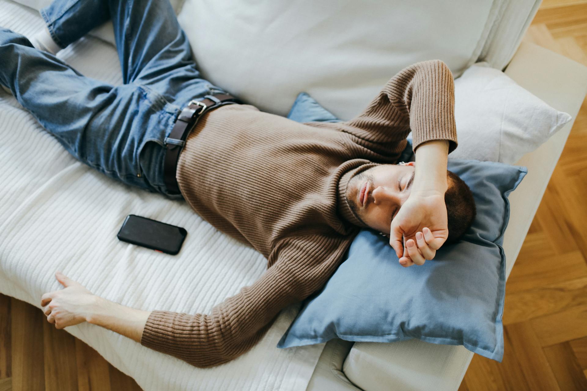 Ein Mann, der auf der Couch schläft und sein Telefon neben sich liegen hat | Quelle: Pexels