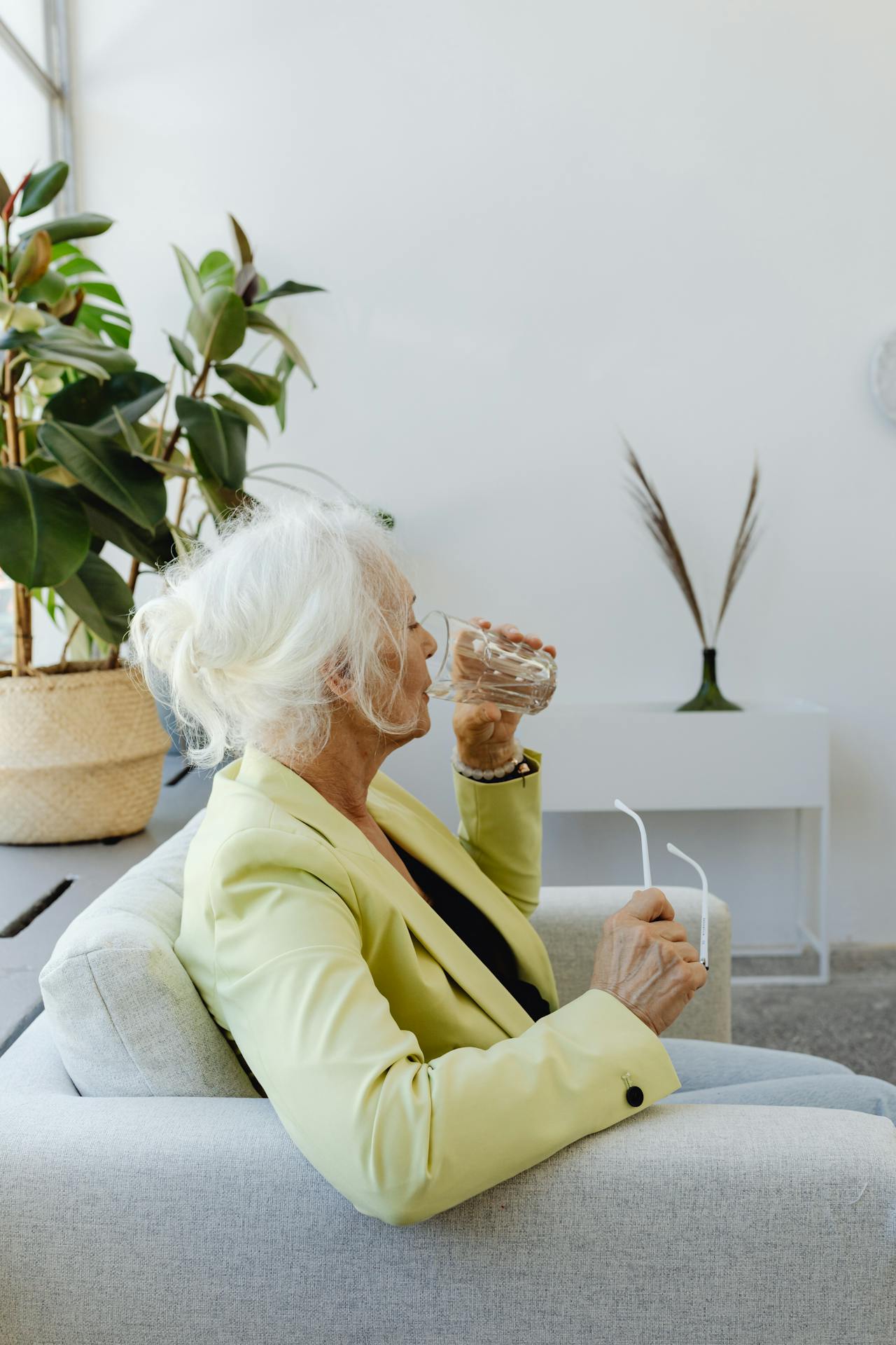 Eine ältere Frau sitzt auf der Couch und trinkt ein Glas Wasser | Quelle: Pexels