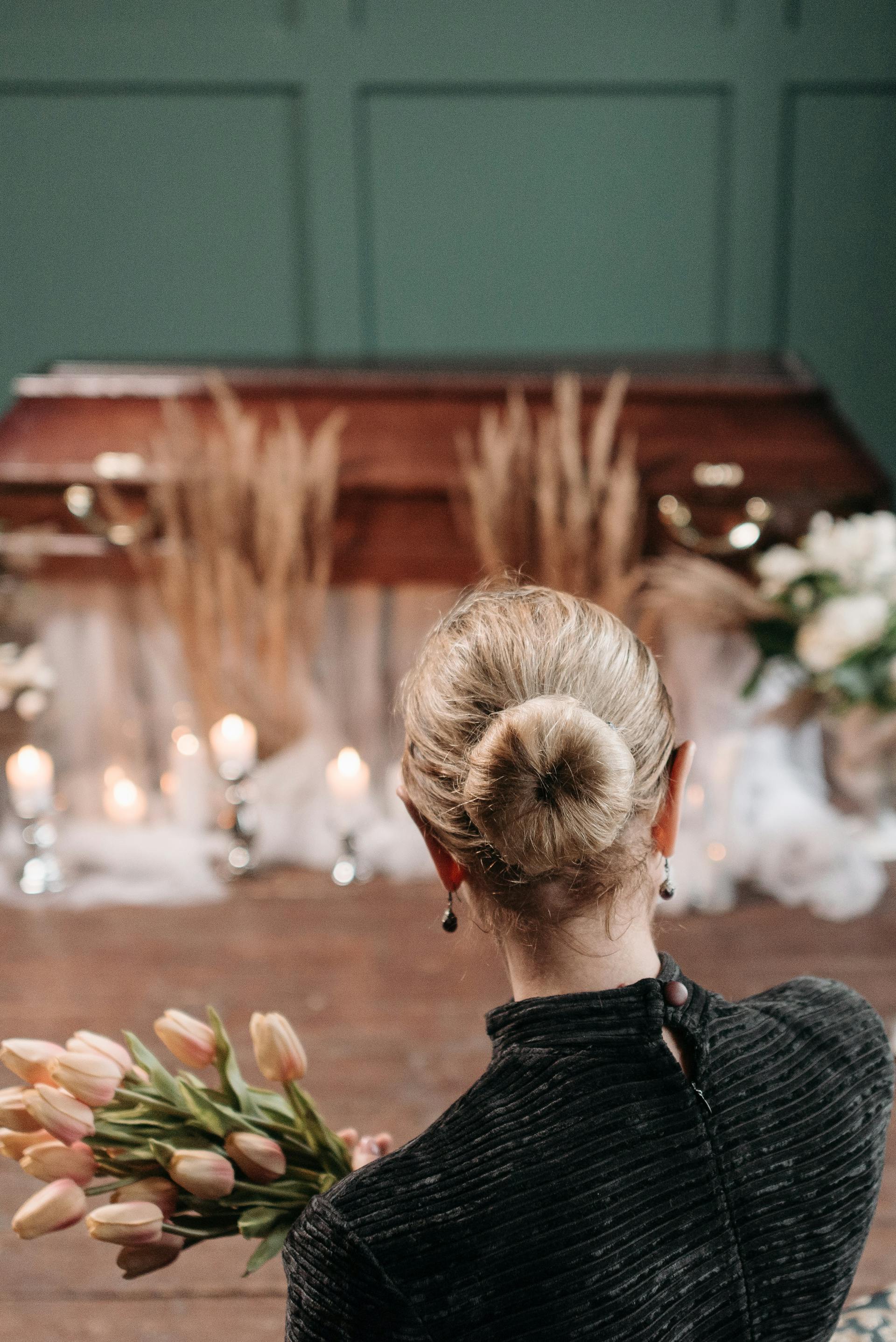 Eine Frau hält einen Blumenstrauß vor einem Sarg | Quelle: Pexels