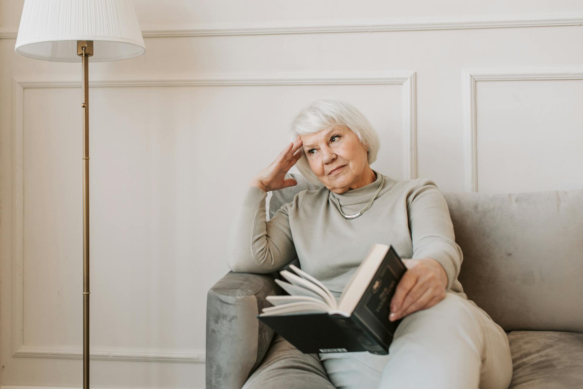 Eine nachdenkliche ältere Frau sitzt mit einem Buch auf einer Couch | Quelle: Pexels