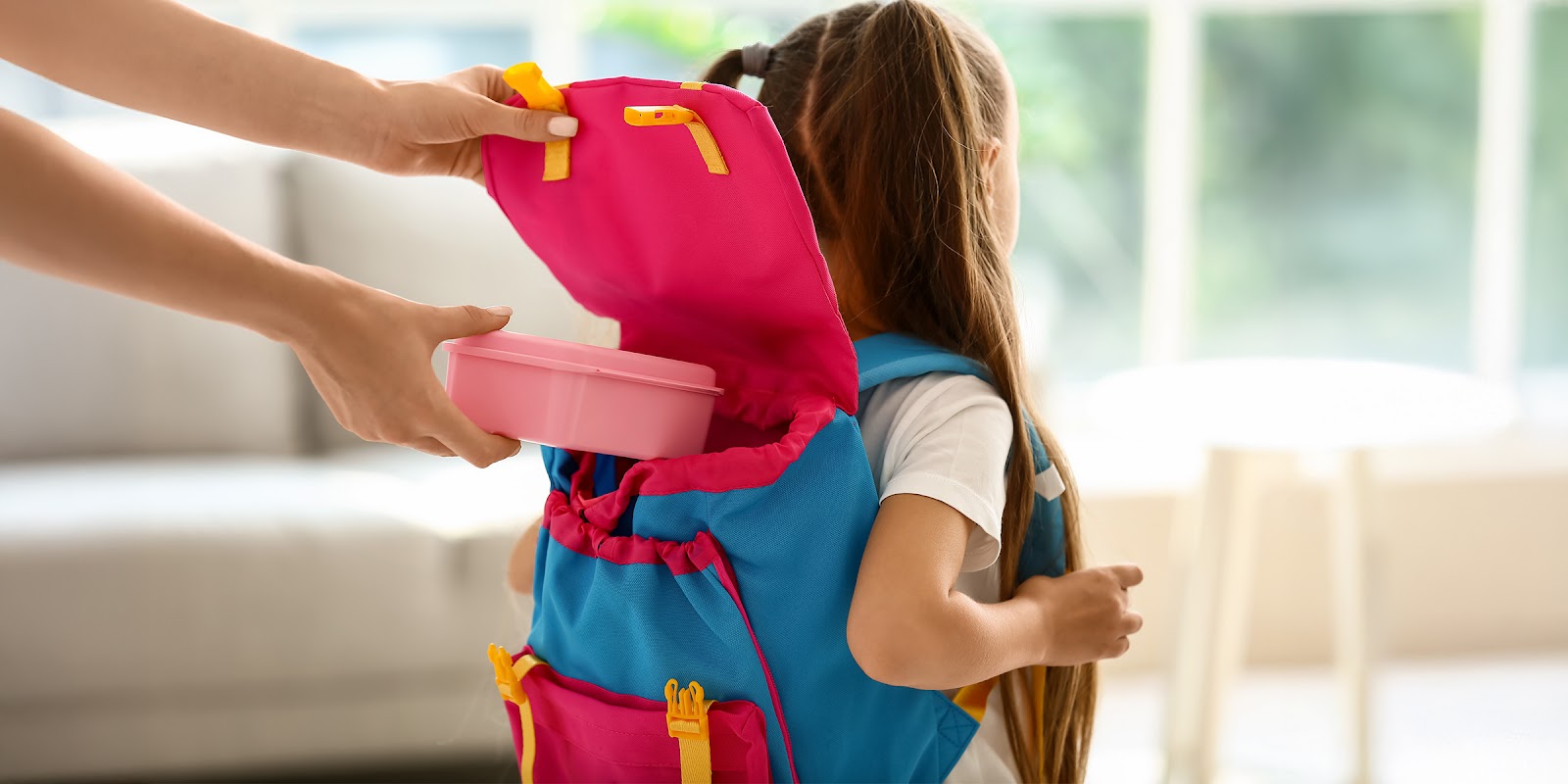 Ein Erwachsener packt eine Brotdose in den Rucksack eines Kindes | Quelle: Shutterstock